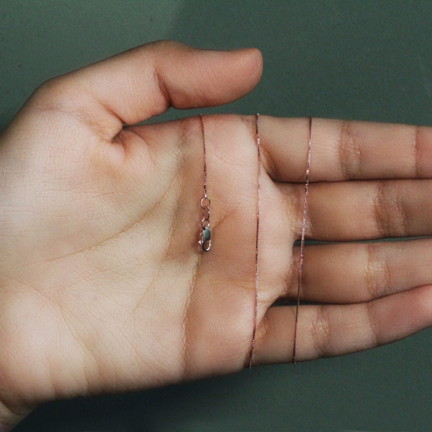 A delicate 14k rose gold box chain with a lobster clasp rests on an open palm.