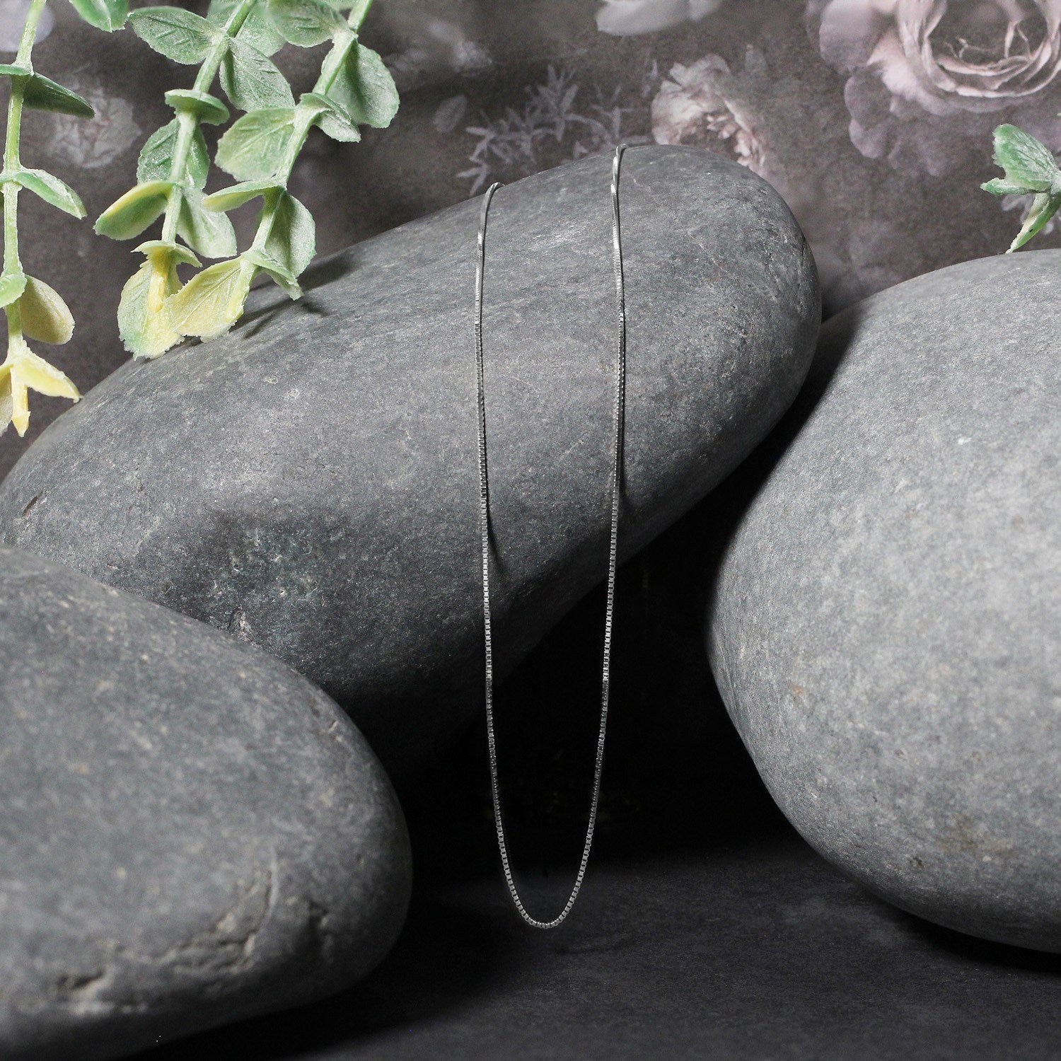 A thin 14k white gold box chain is draped over smooth gray stones.