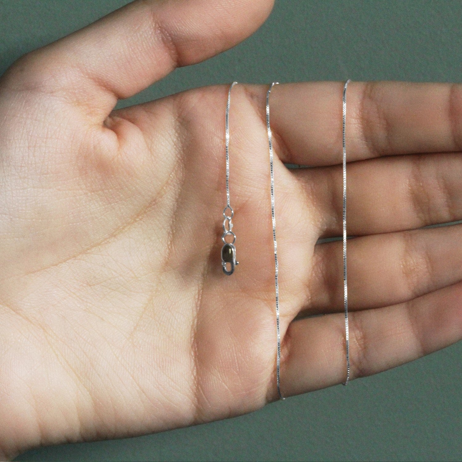 A 14k white gold classic box chain with a lobster clasp is held in a hand.