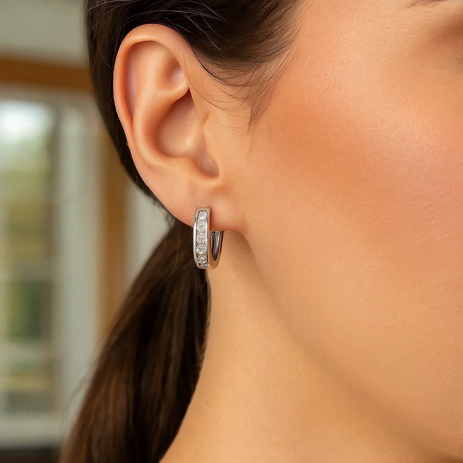 Sterling silver oval hoop earrings with cubic zirconias on a woman's ear.
