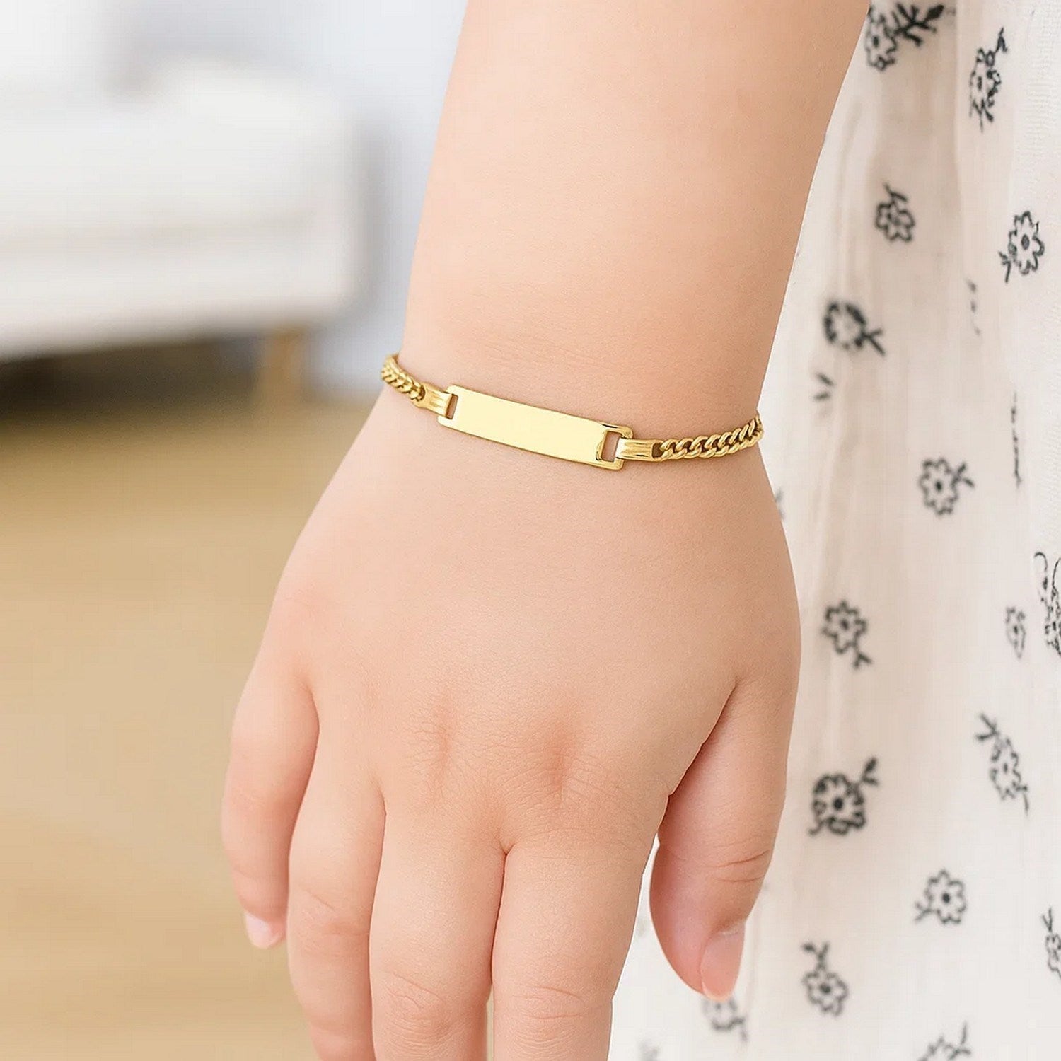 A child's arm wears a 14k yellow gold curb link ID bracelet.