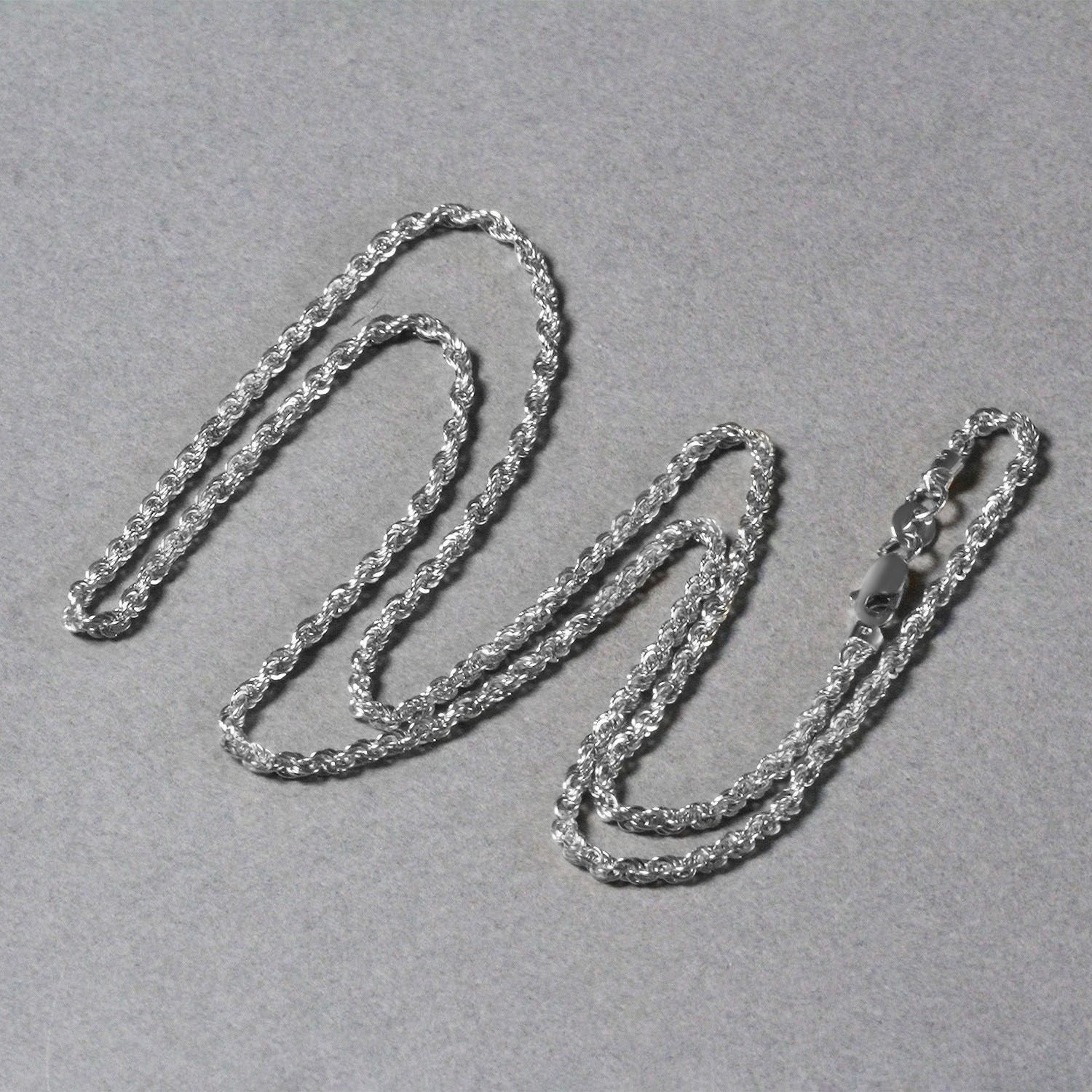 A 14k white gold light rope chain with a lobster clasp, laid on a gray surface.
