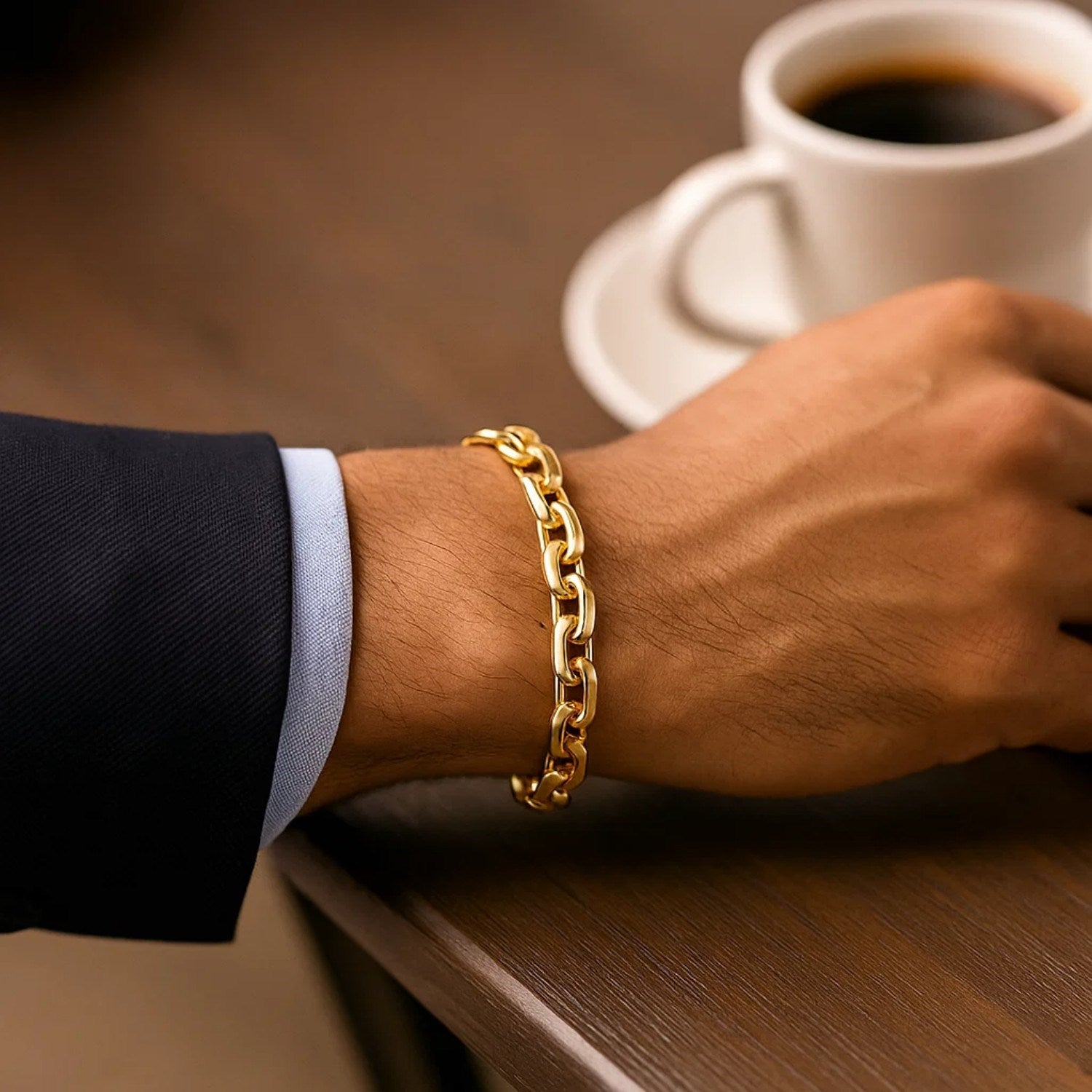 14k yellow gold French cable chain bracelet on a man's wrist with a coffee cup in the background.