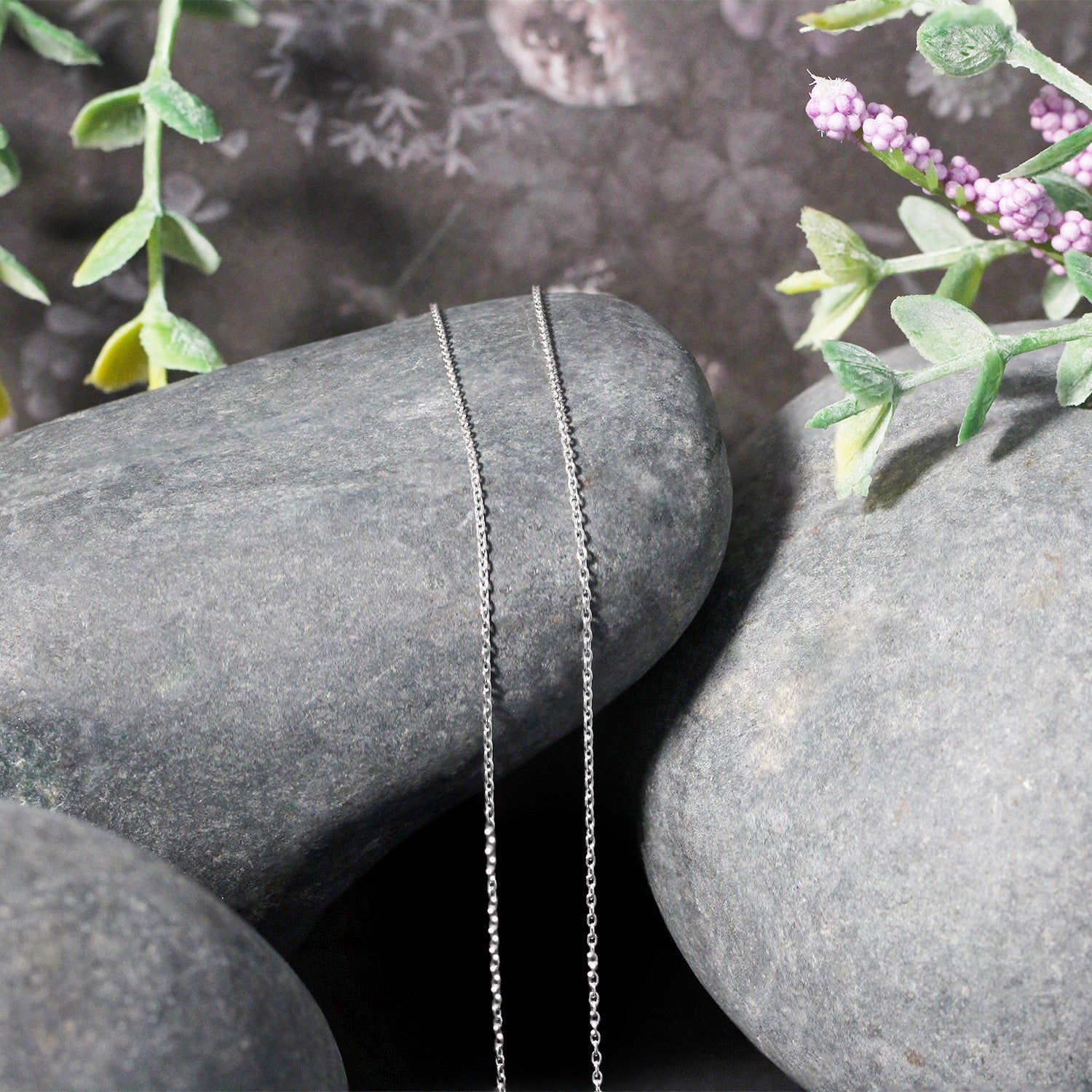 A 10k white gold oval cable link chain, 0.97 mm wide, draped over grey stones.