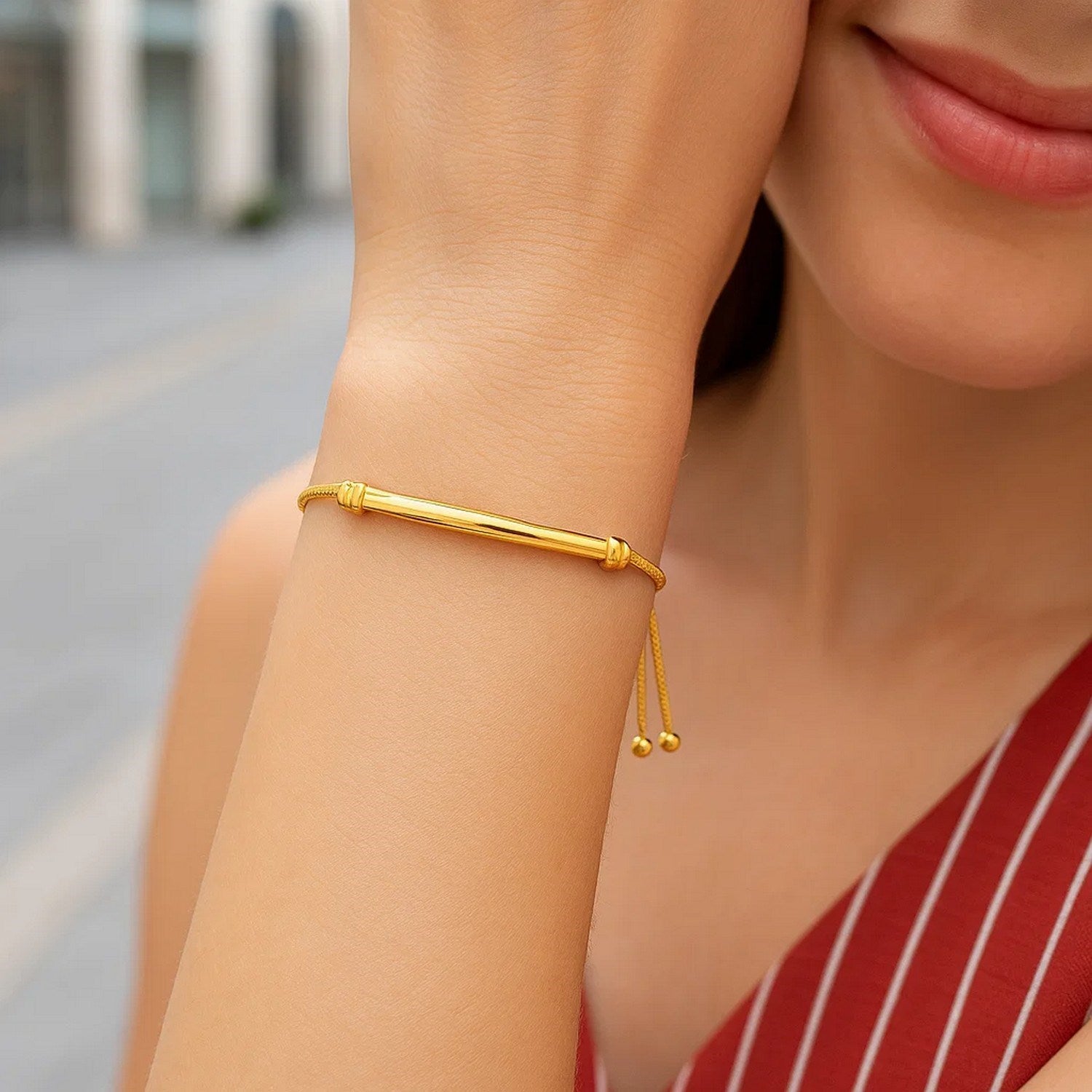 14k yellow gold smooth curved bar and lariat style bracelet on a woman's wrist.