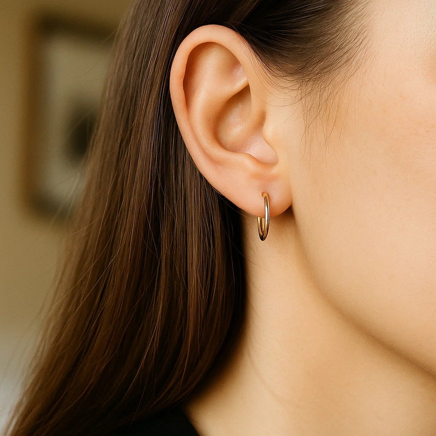 A woman wears a single polished 10k yellow gold endless hoop earring.