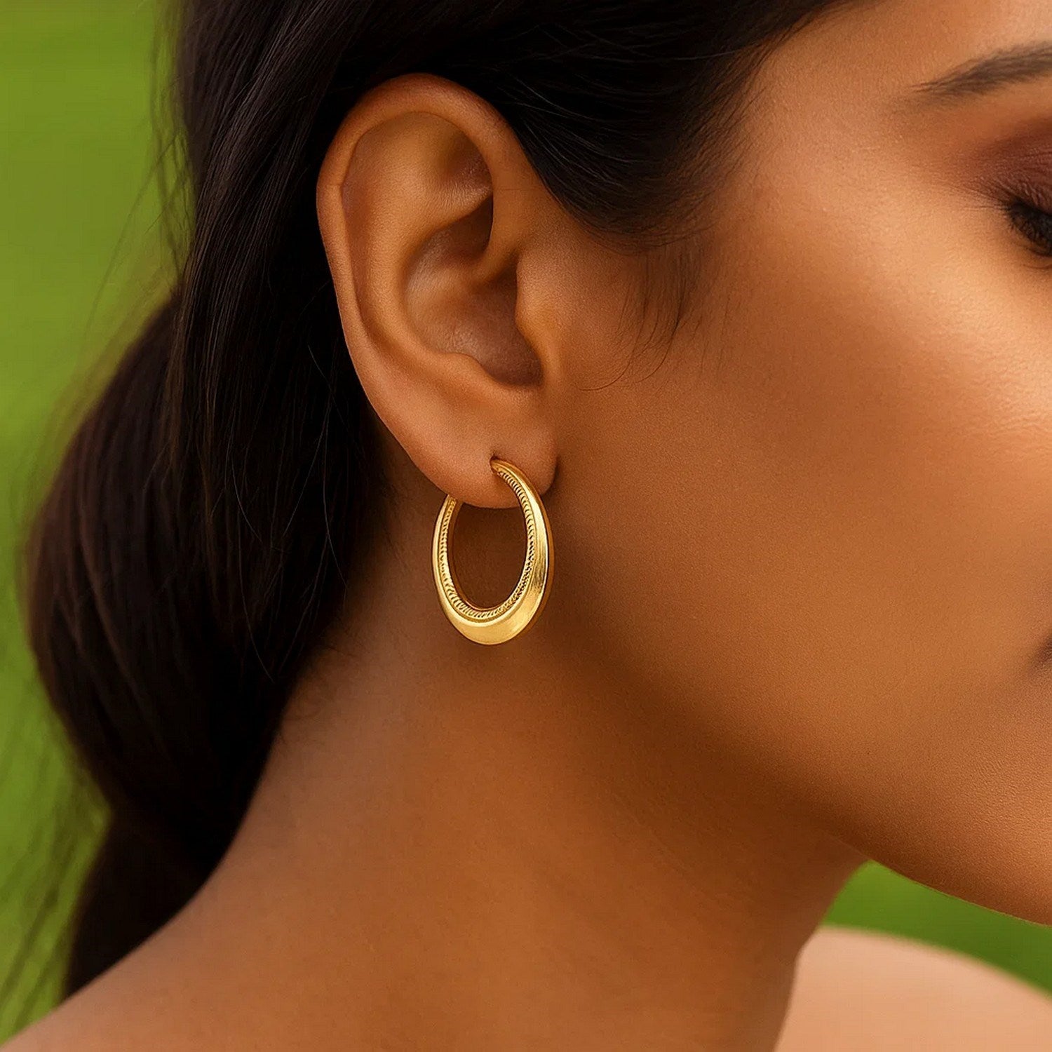 14k yellow gold round hoop earrings with rope texture detailing on a person's ear.
