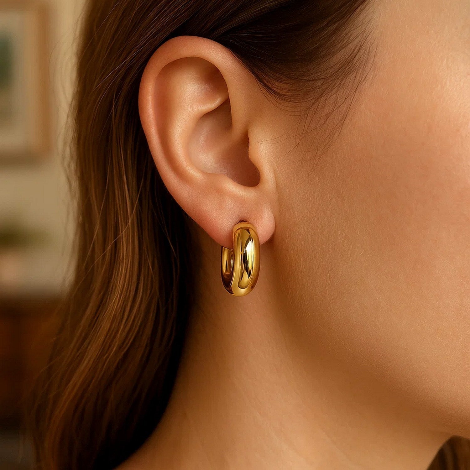 A woman wears a single 14k yellow gold small puffy hoop earring.
