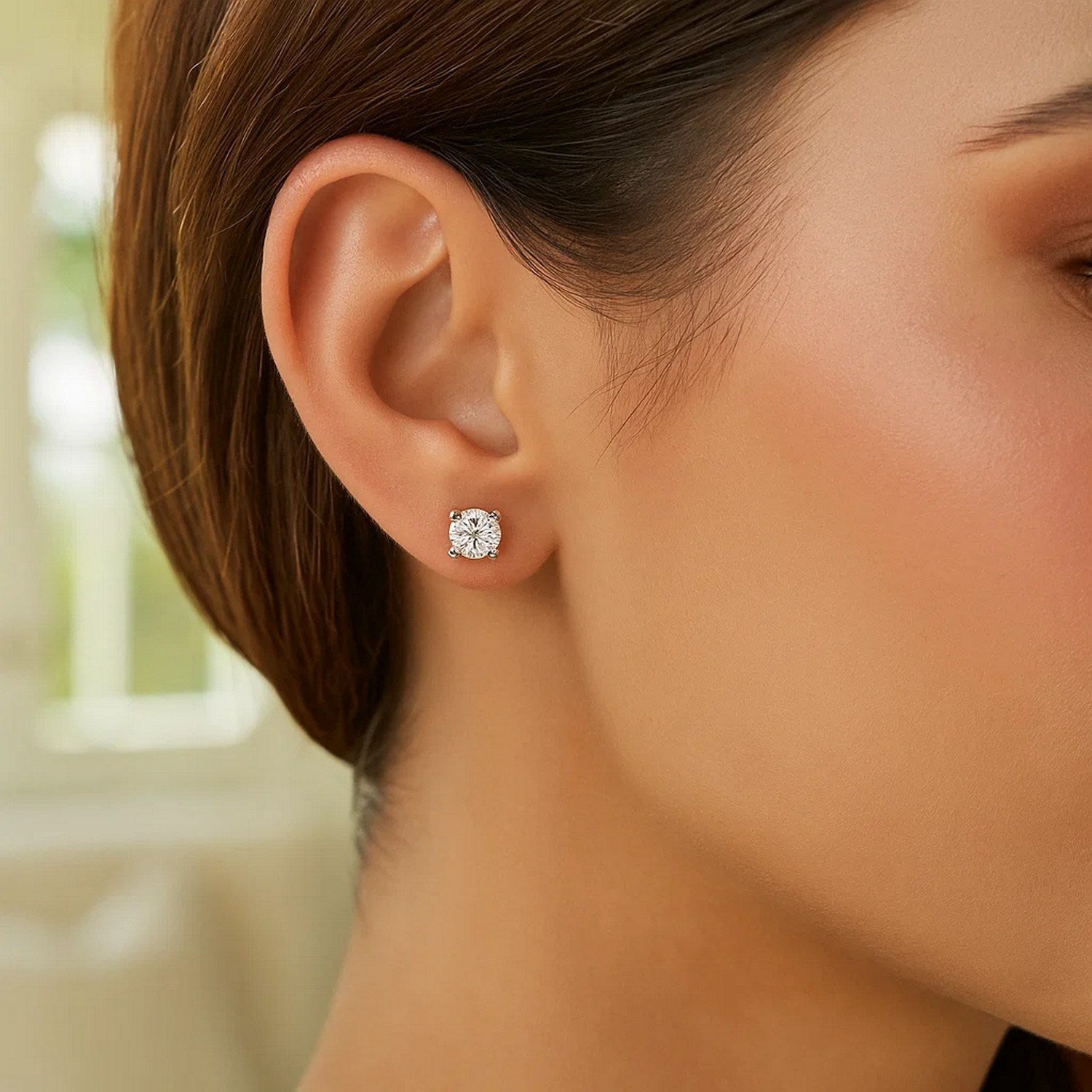 A woman wears a single sterling silver stud earring with a white cubic zirconia.