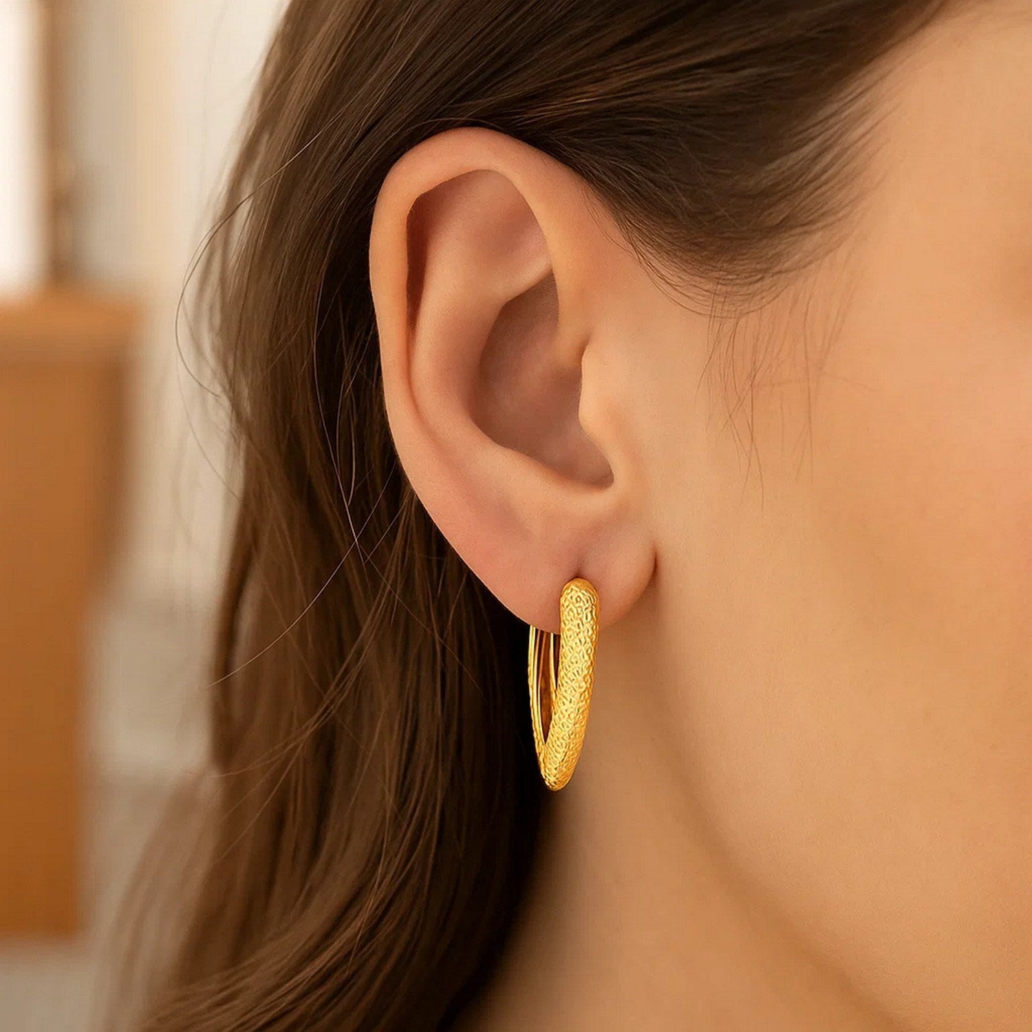 14k yellow gold V-shaped puffed hoop earring with a textured finish on a woman's ear.