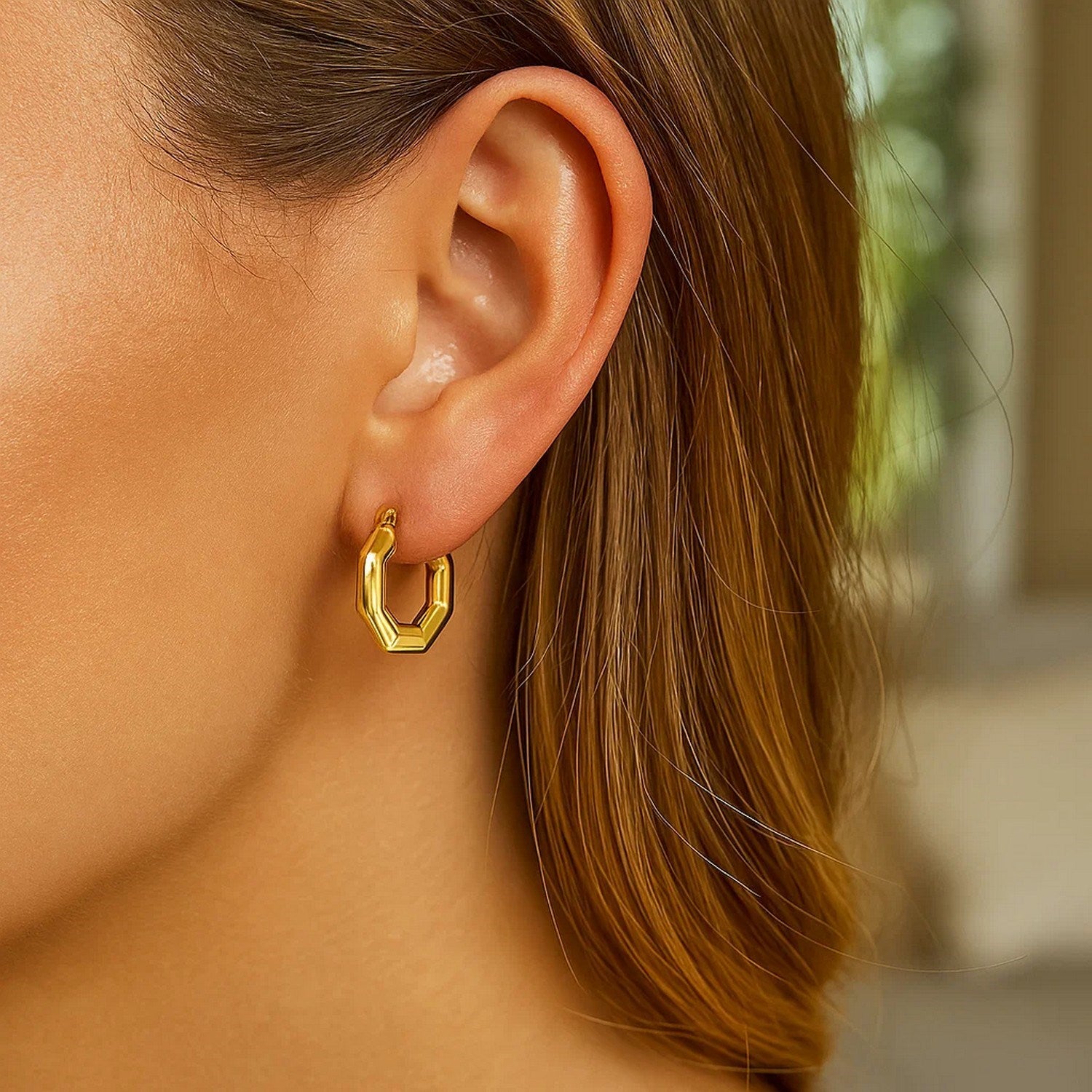 A woman wears a single 14k yellow gold octagon hoop earring.