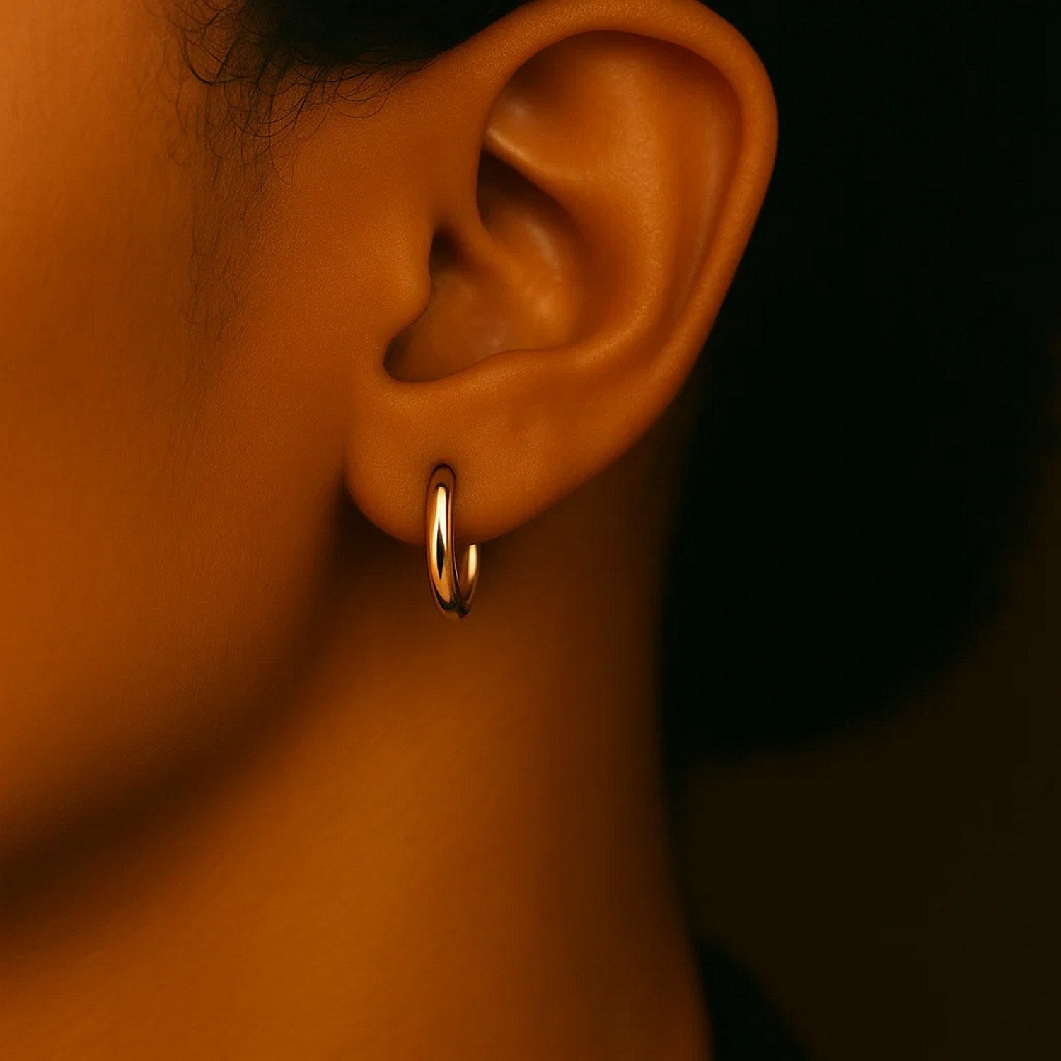 A close-up of a person's ear wearing a single polished yellow gold hoop earring.