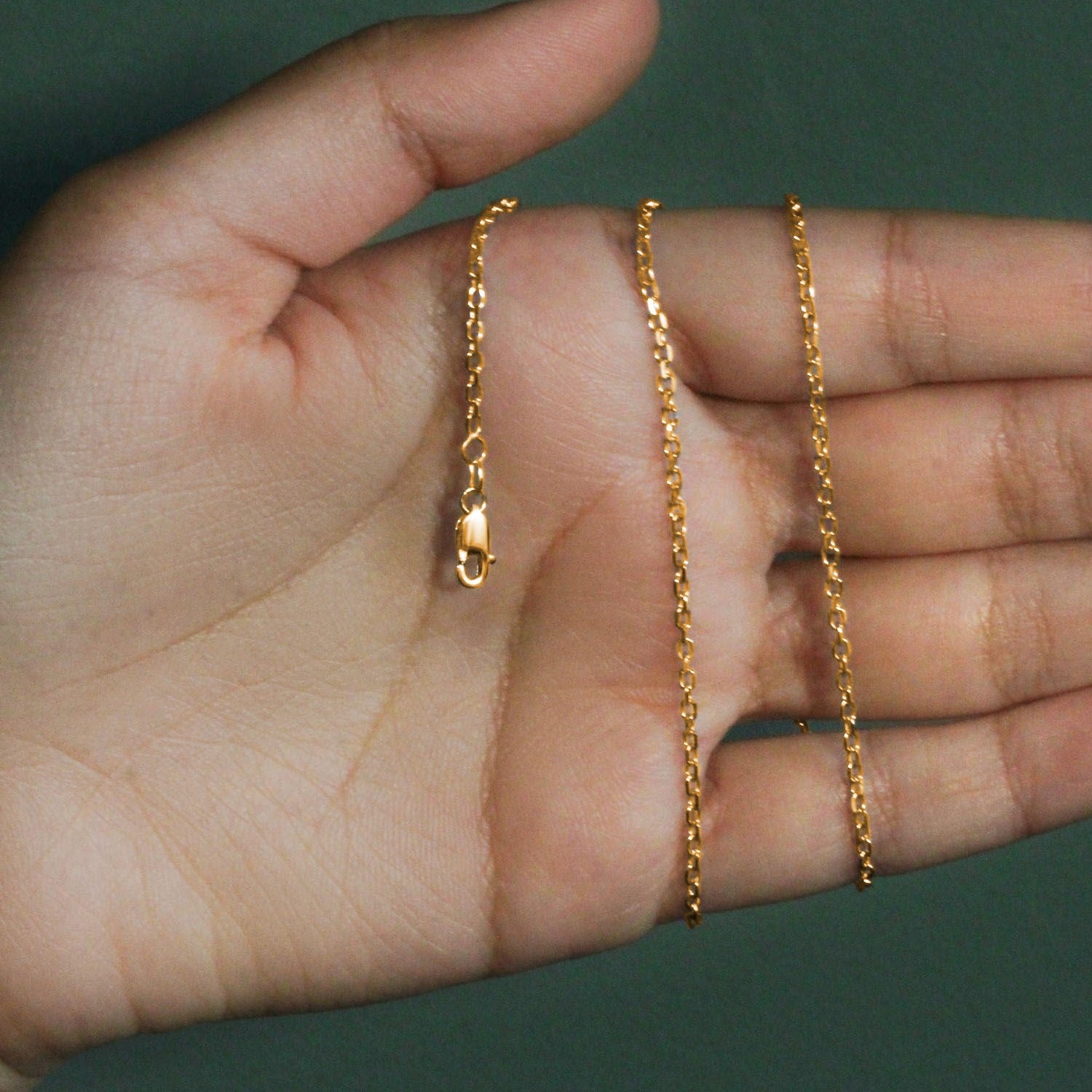 18k yellow gold diamond cut cable link chain with a lobster clasp on a hand.