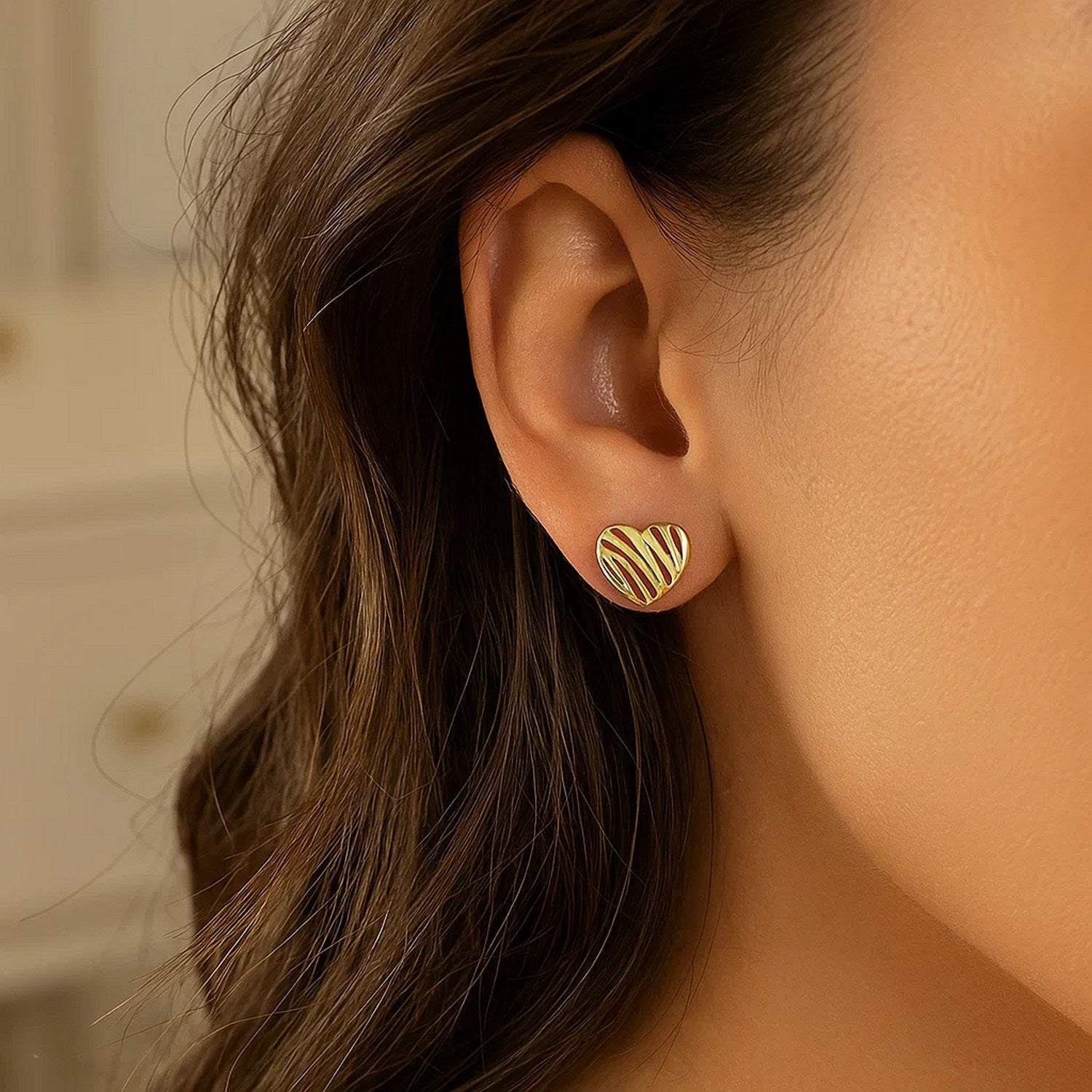 14K yellow gold high polish scribble heart stud earrings on a woman's ear.