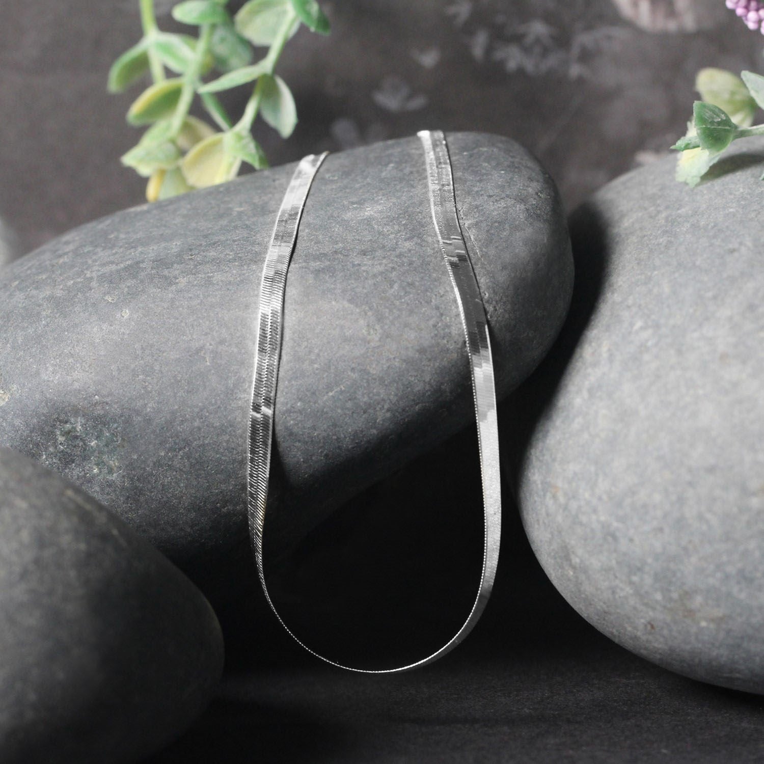 A 14k white gold super flex herringbone chain rests on dark gray stones.