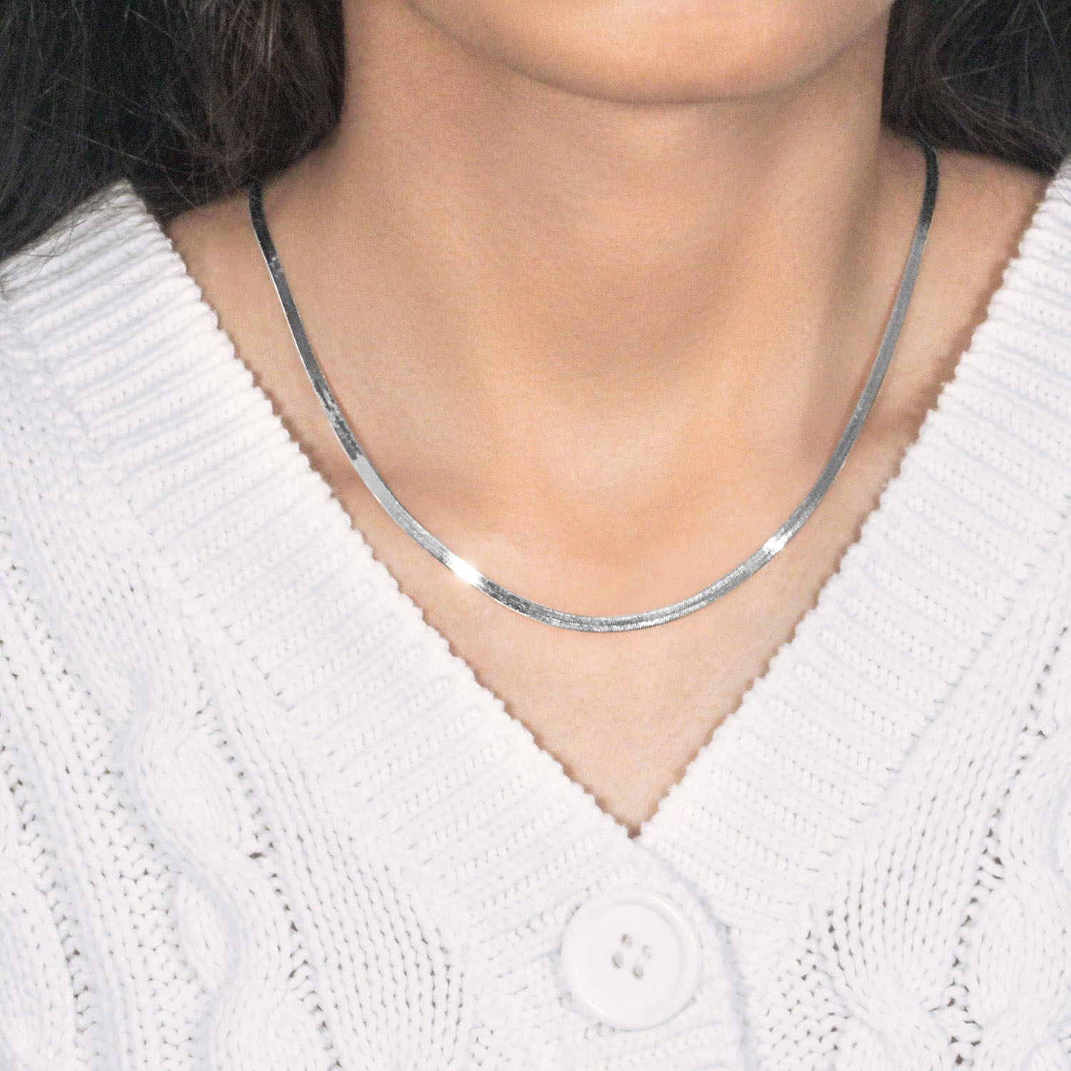 A 14k white gold super flex herringbone chain is worn around a person's neck.