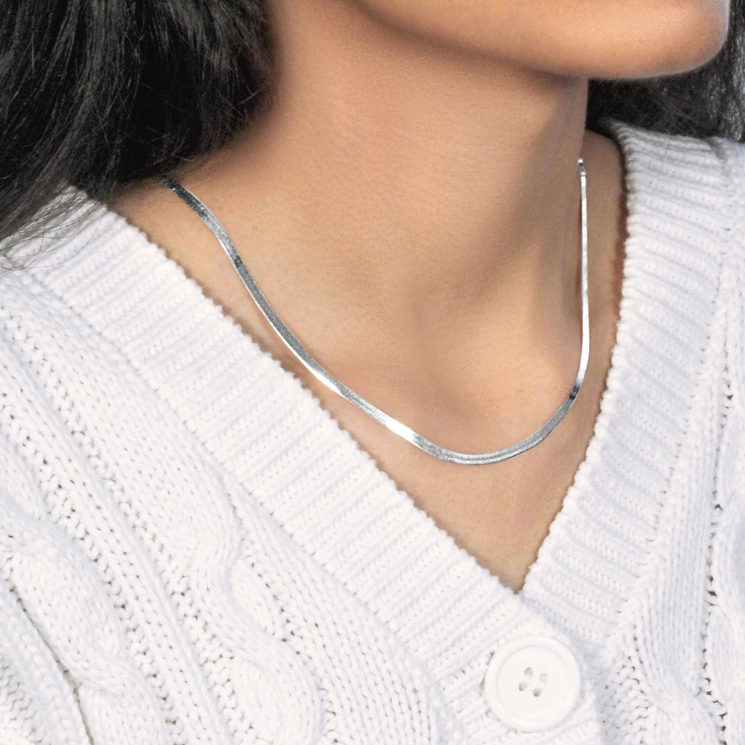 A 14k white gold super flex herringbone chain on a person wearing a white sweater.