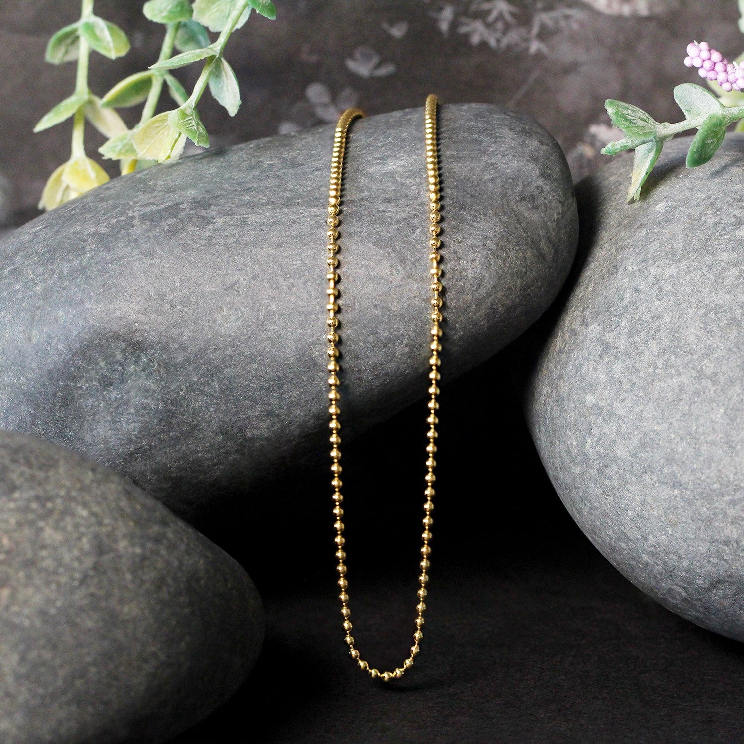 14k yellow gold 1.5mm bead chain draped over dark grey stones.