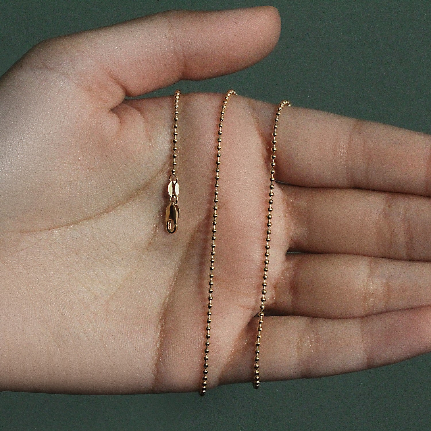 14k yellow gold 1.5mm bead chain with a lobster clasp held in a hand.