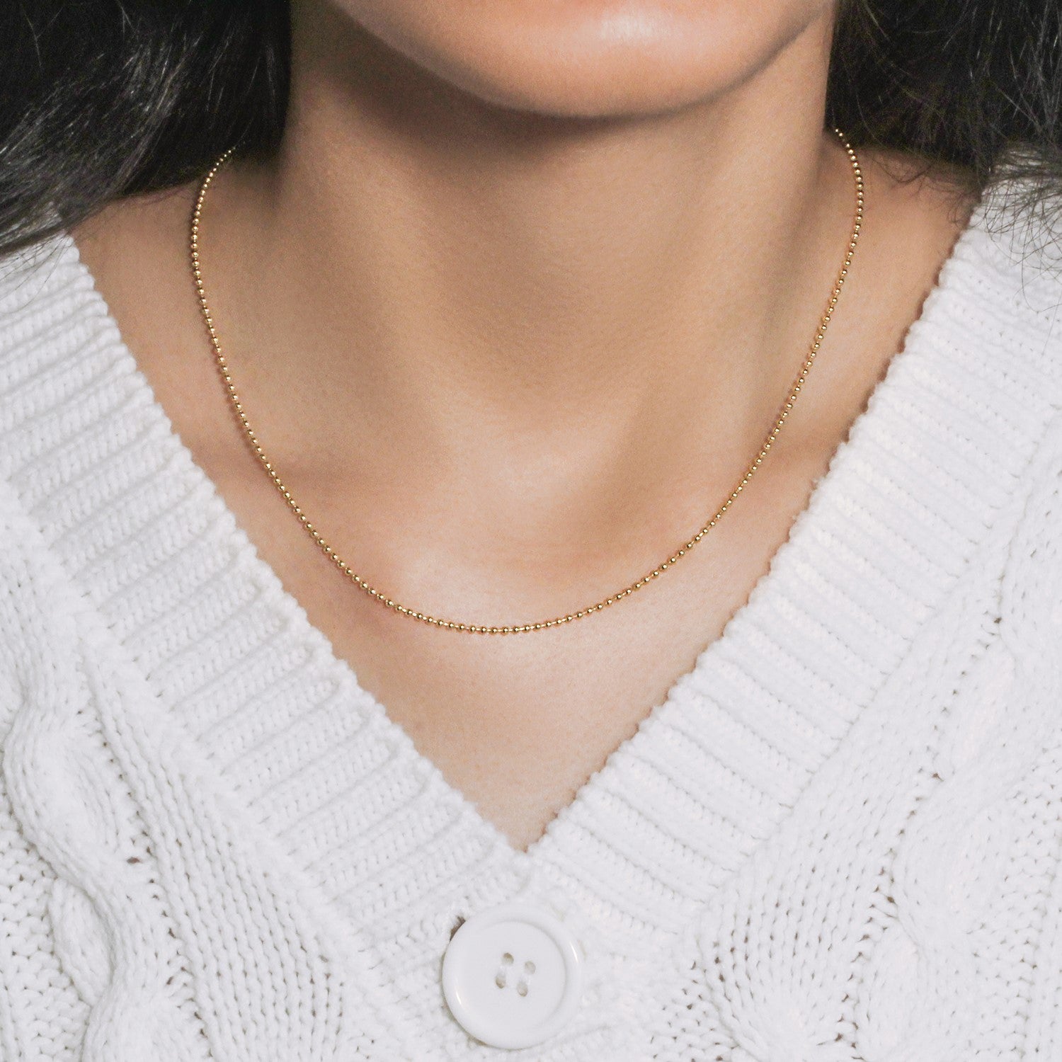 14k yellow gold 1.5mm bead chain on a person wearing a white cable knit sweater.