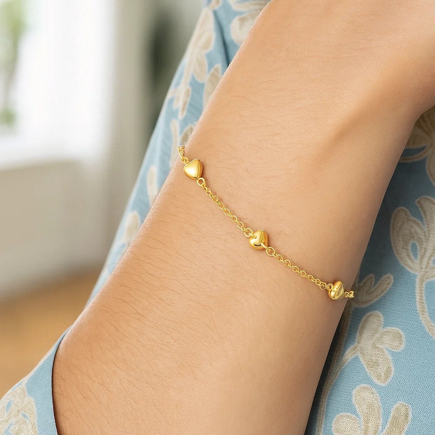 A 14k yellow gold rolo chain bracelet with three puffed heart stations is worn on an arm.