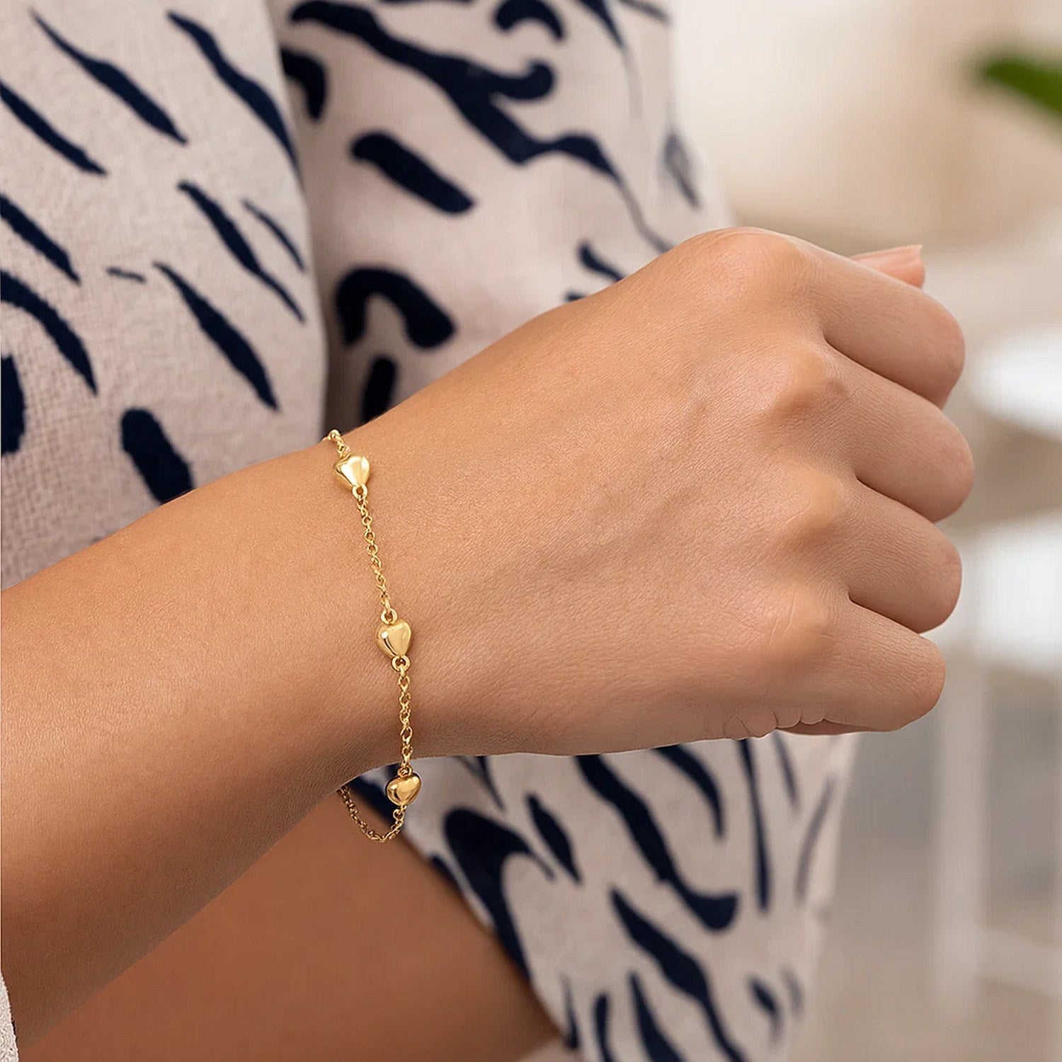 14k yellow gold rolo chain bracelet with puffed heart stations on a person's wrist.