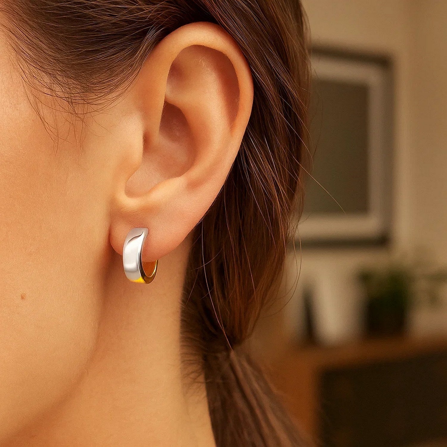 A woman wears a two-tone gold snuggable style hoop earring.