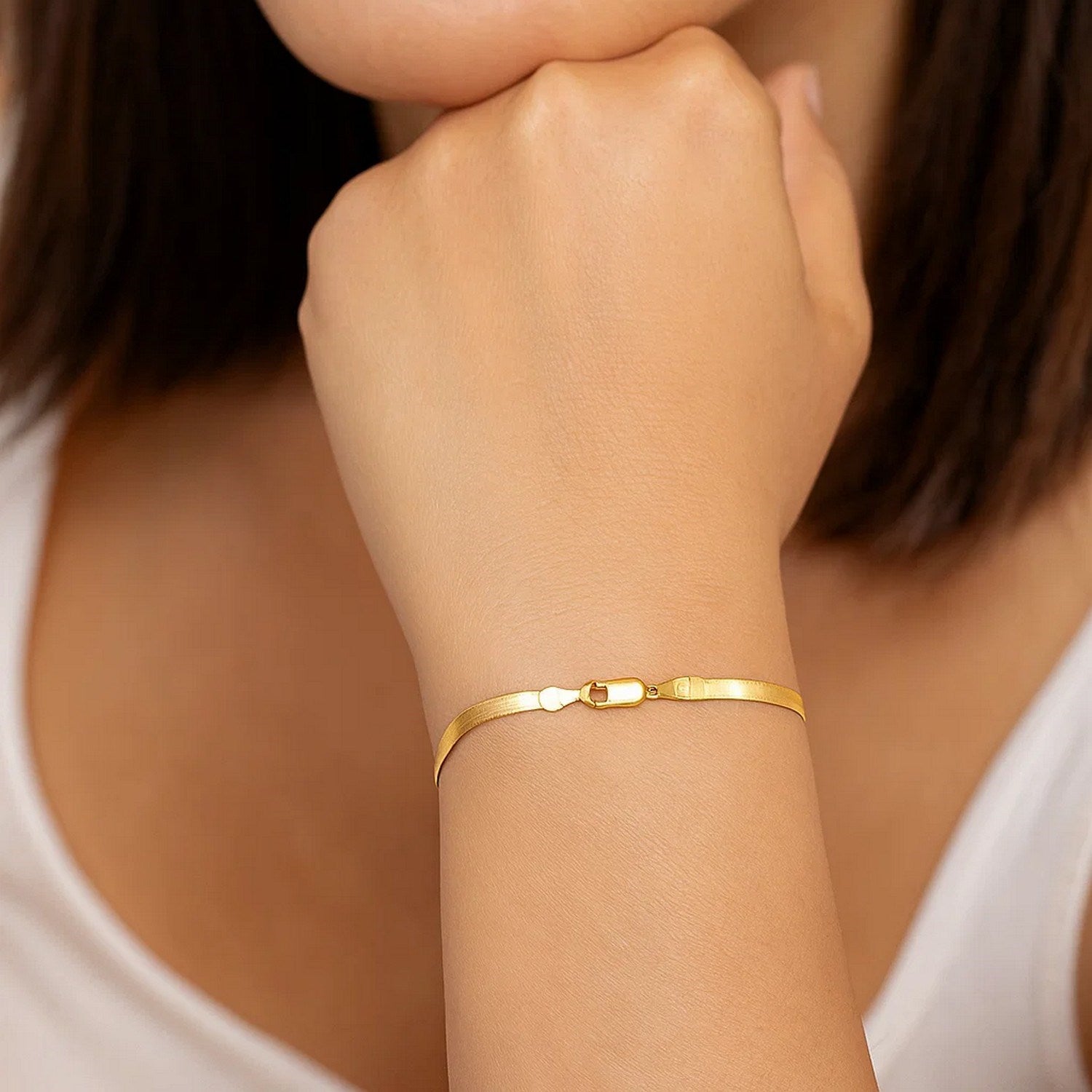 14k yellow gold super flex herringbone bracelet with a lobster clasp on a woman's wrist.