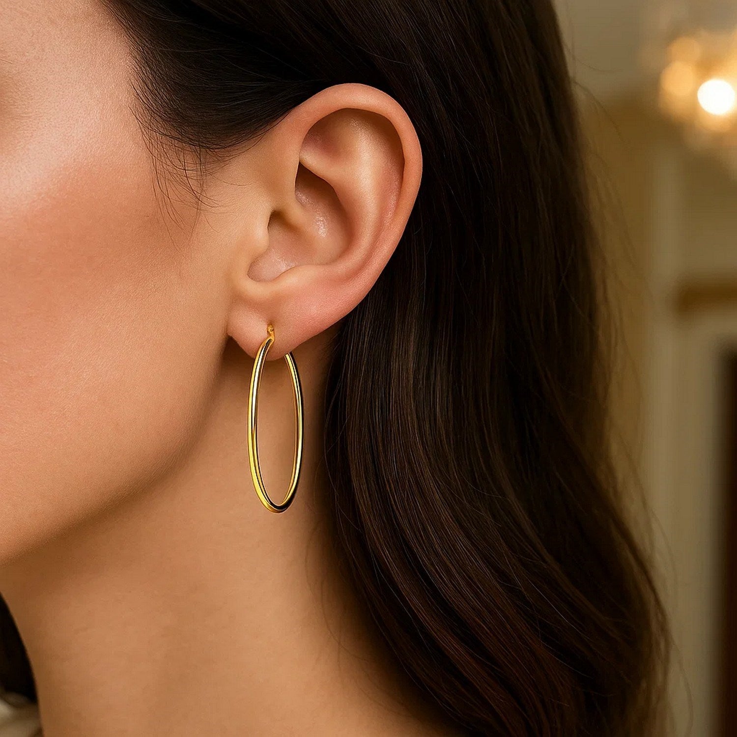 14k yellow gold slim oval shape hoop earrings on a woman's ear.