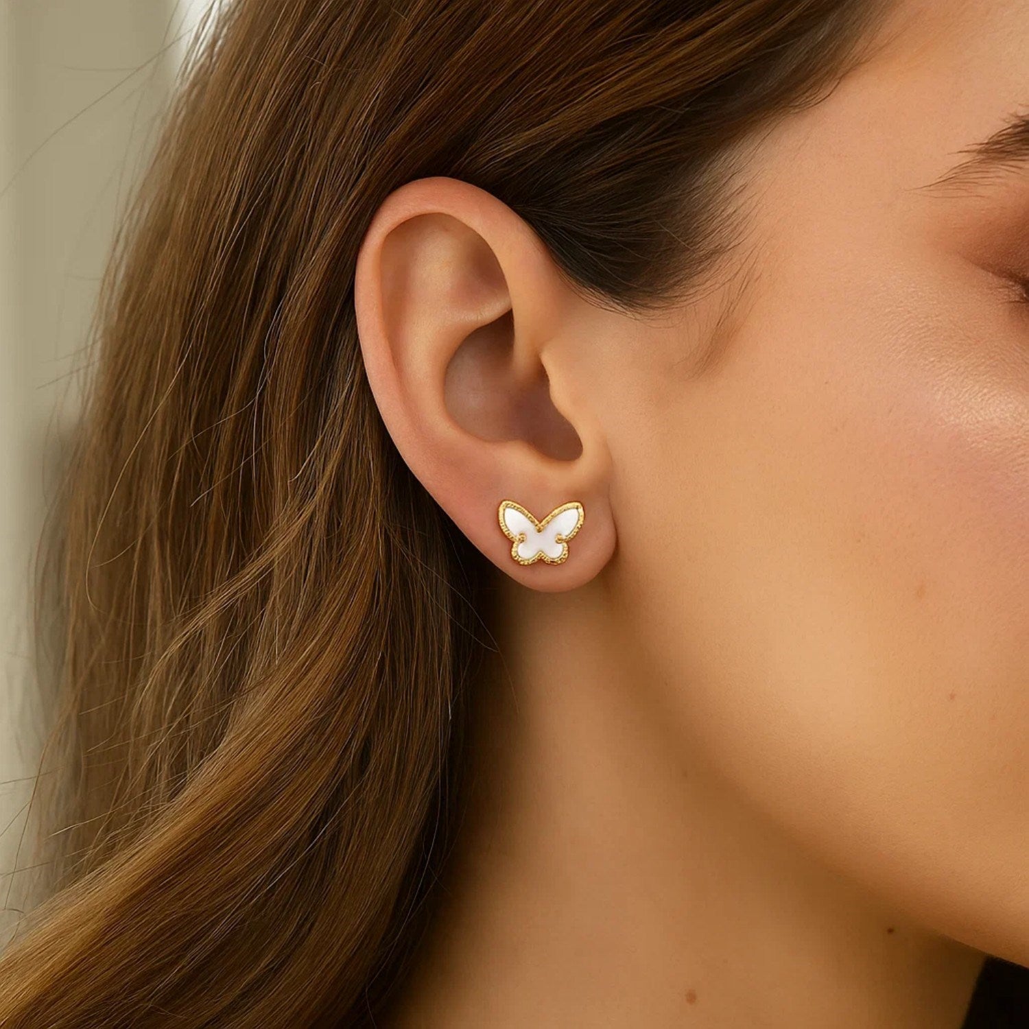 A woman wears a 14K yellow gold mother of pearl butterfly stud earring.