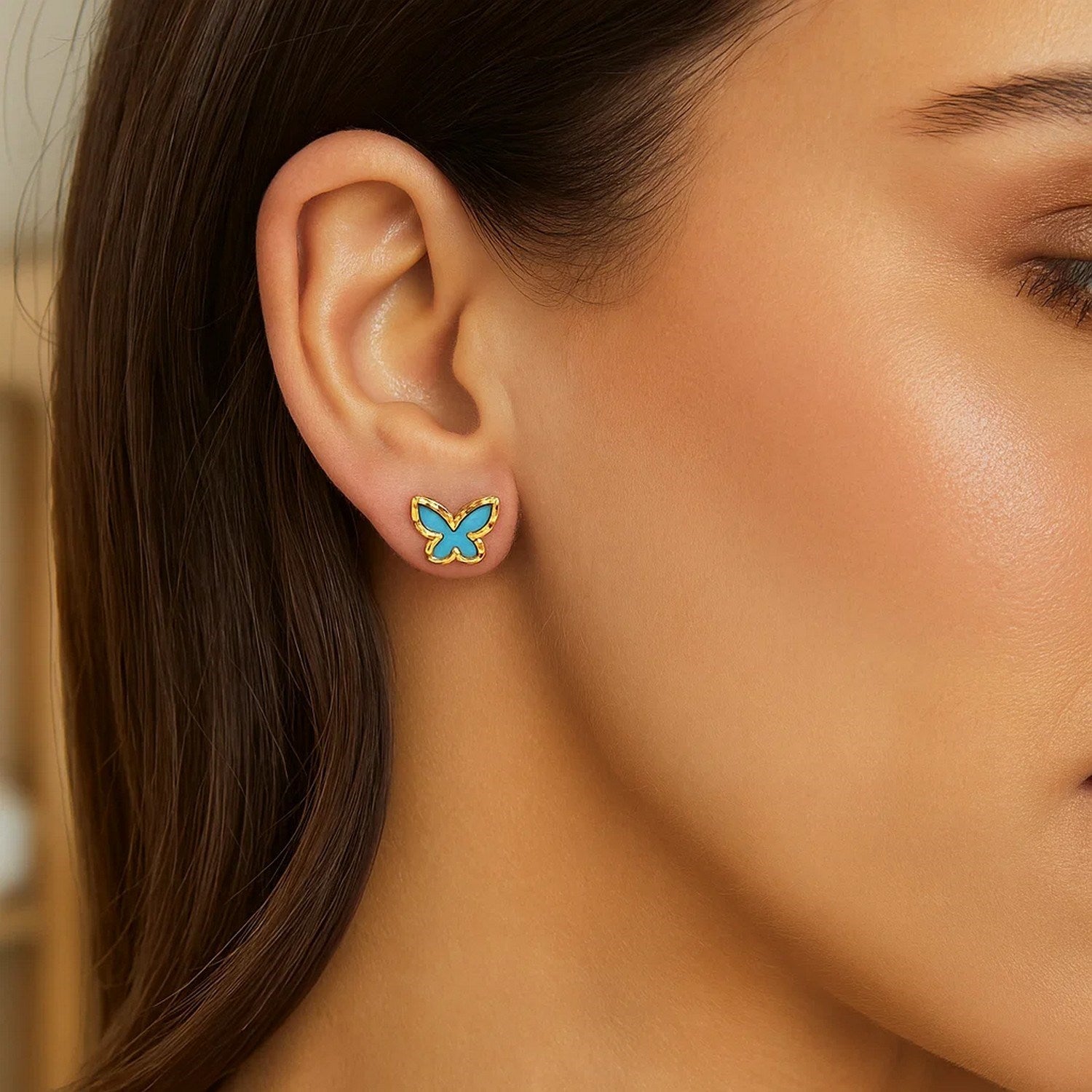 14K yellow gold butterfly stud earrings with turquoise inlay on a woman's ear.