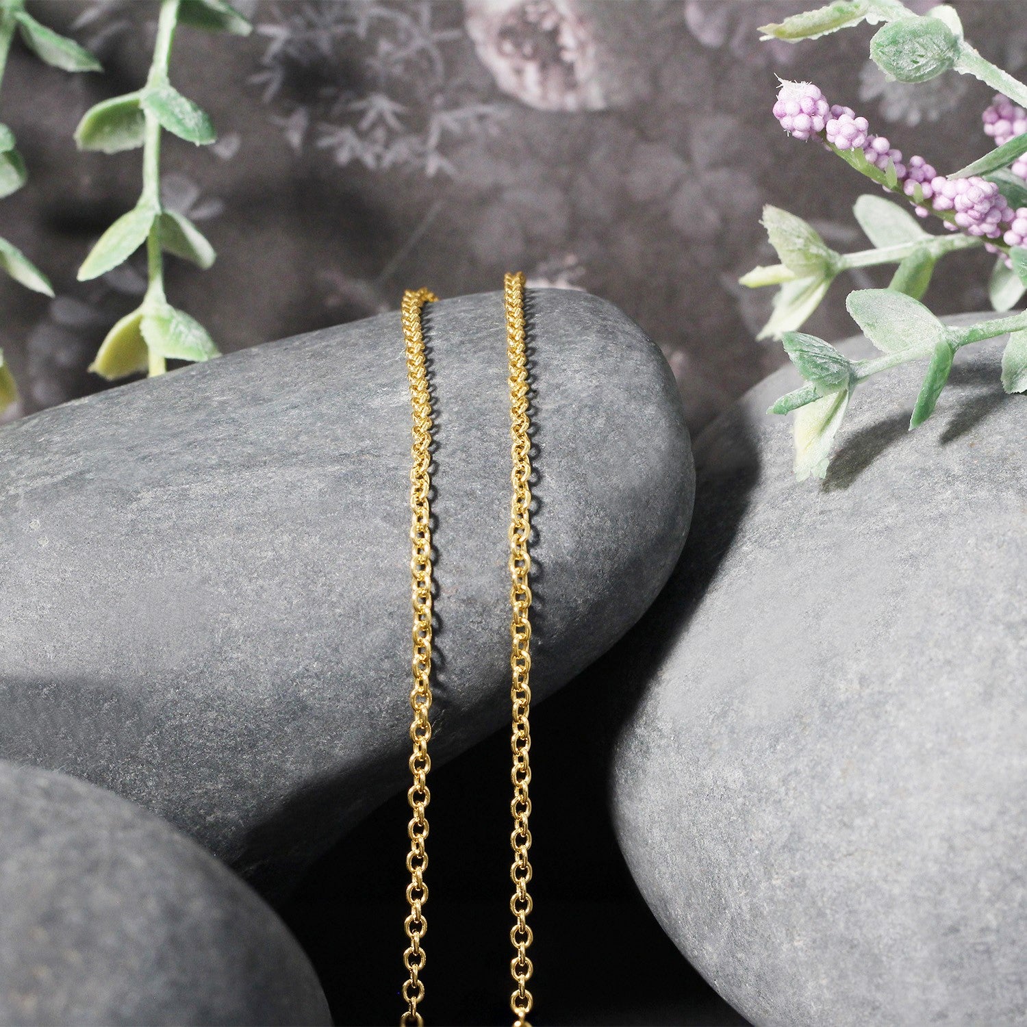 A 14k yellow gold round cable link chain is draped over smooth gray stones.