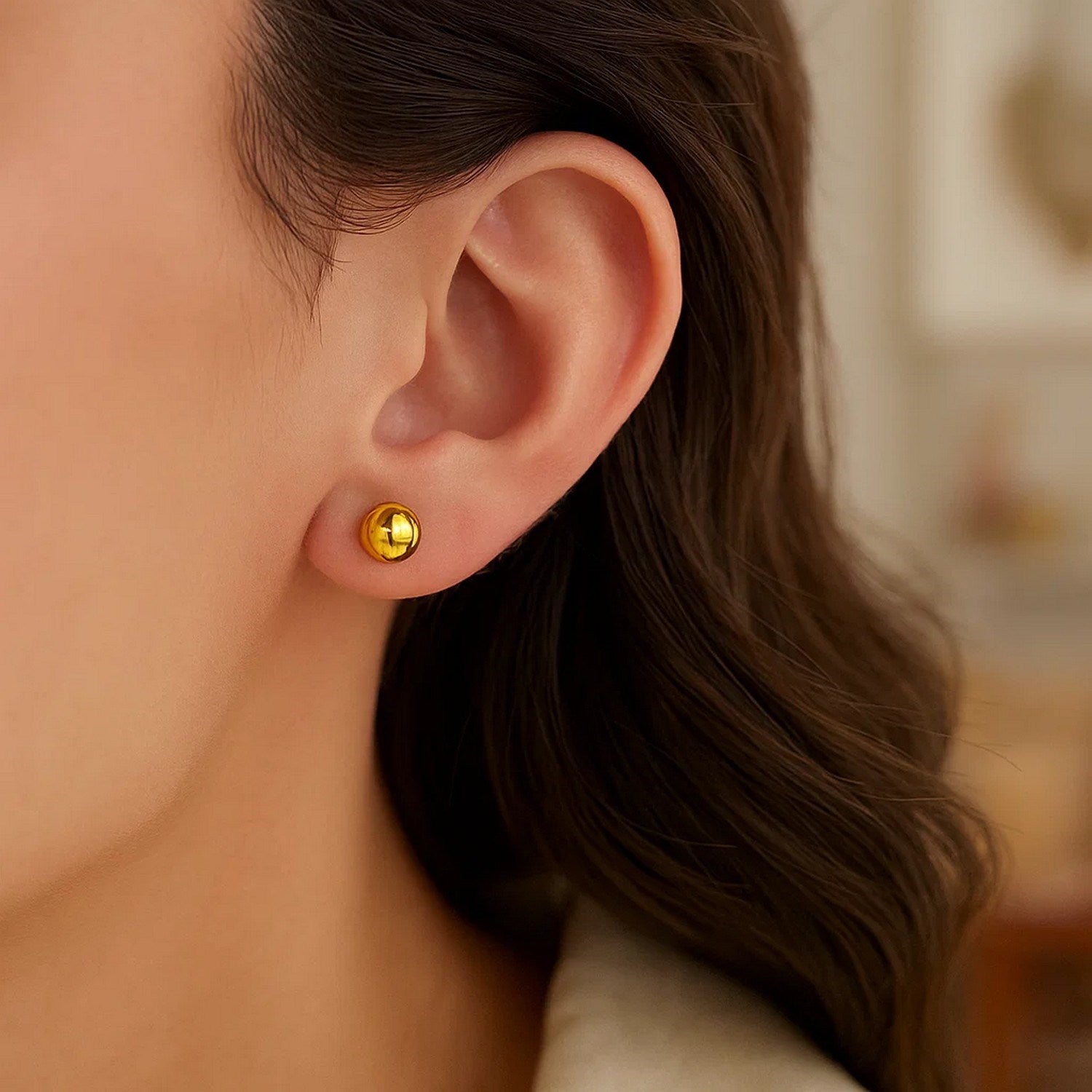 A close-up of a woman wearing a single 14k yellow gold round stud earring.