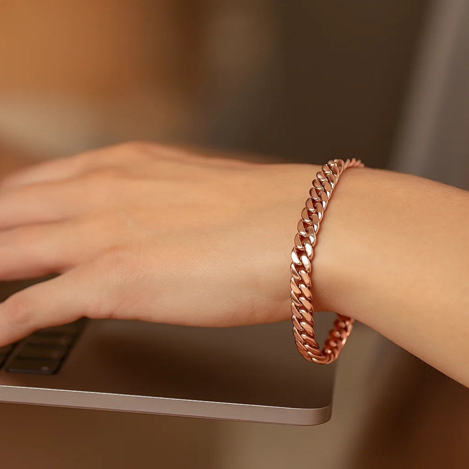 14K rose gold Cuban link bracelet on a person's wrist while typing on a laptop.