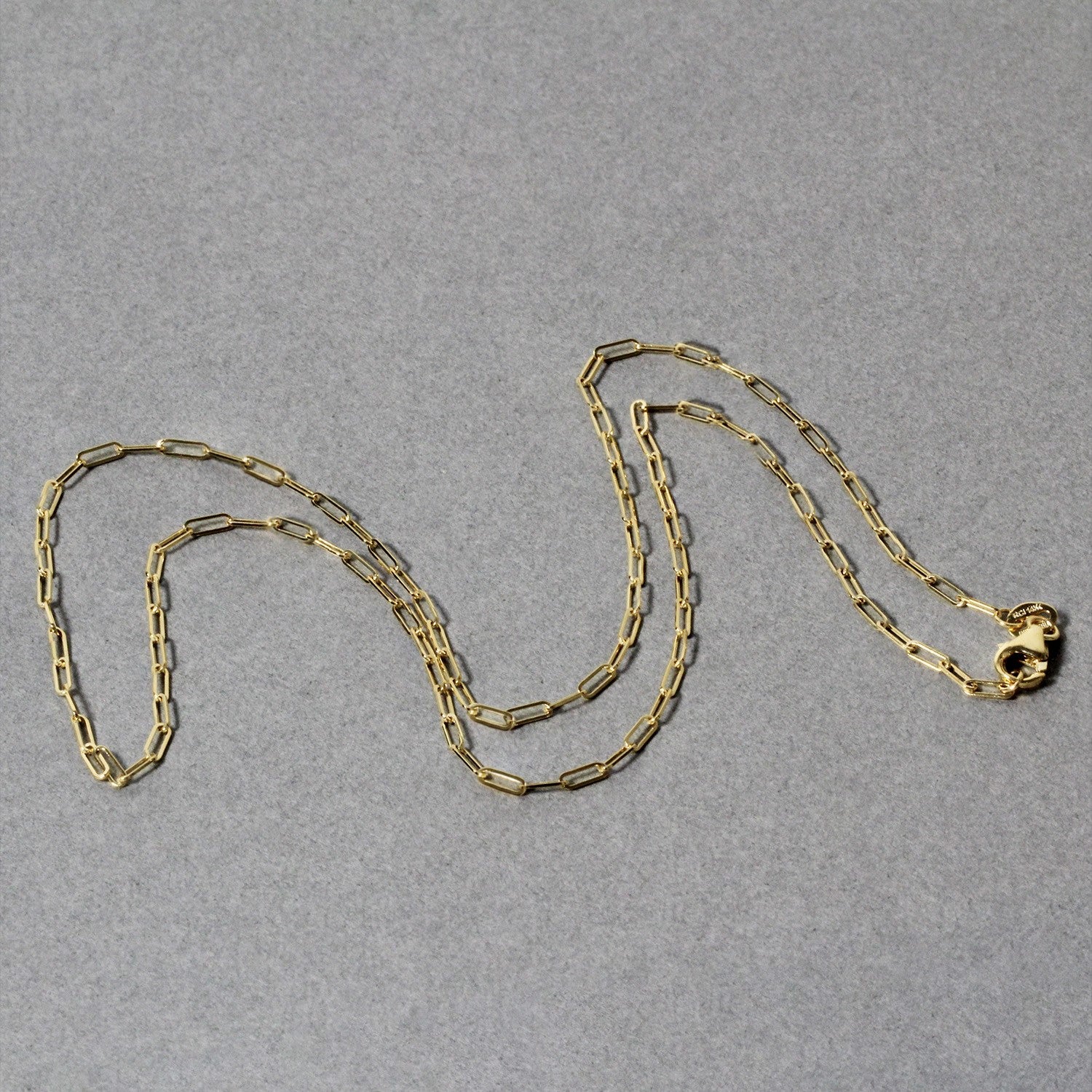 18K yellow gold fine paperclip chain with a lobster clasp on a gray background.