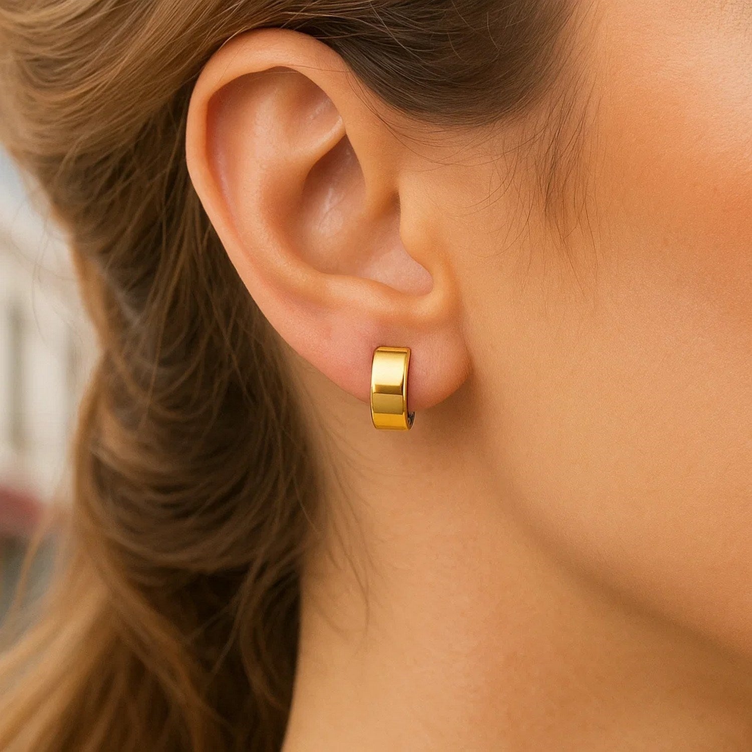 A woman wears a single polished gold hoop earring on her earlobe.