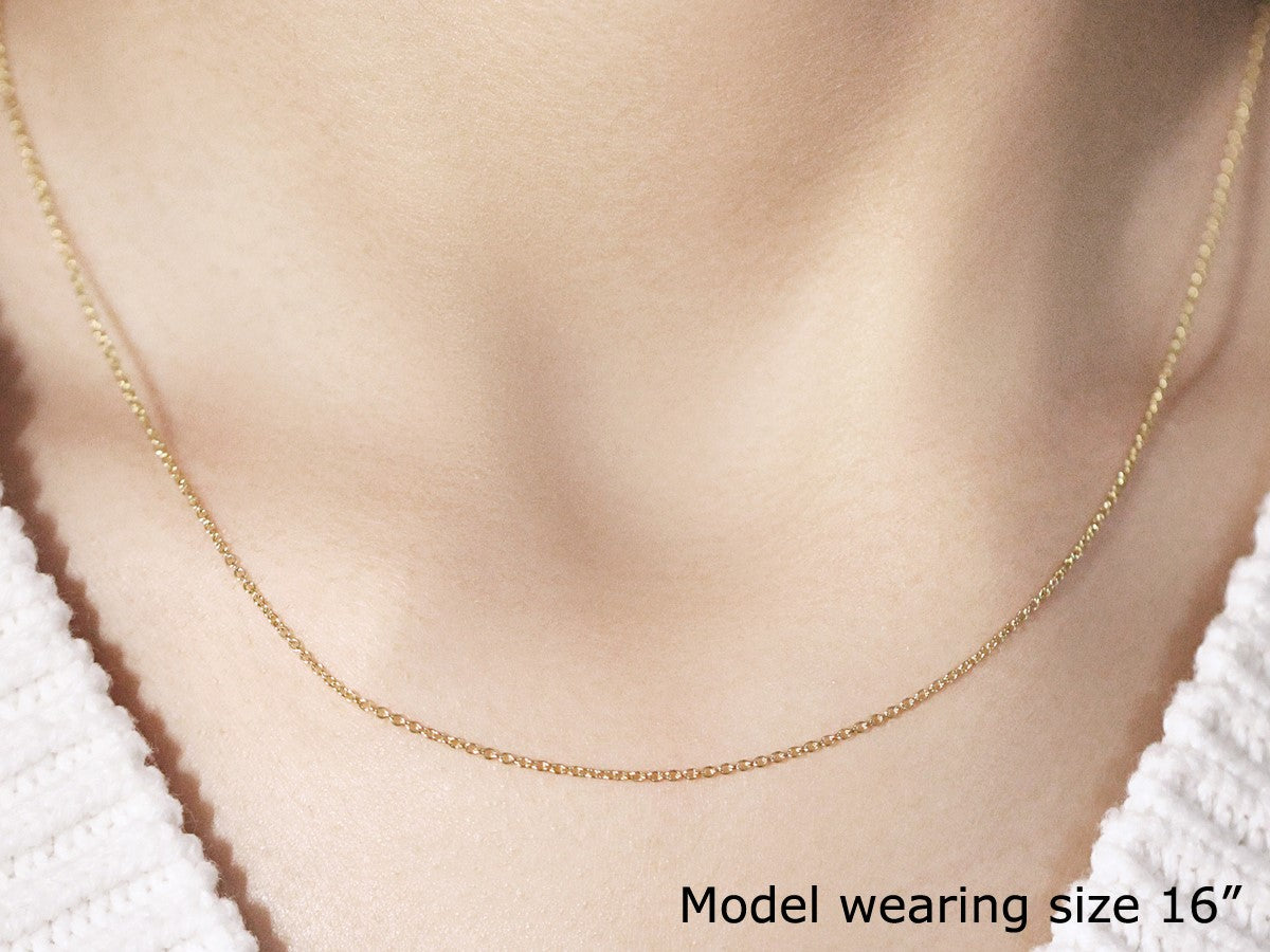 A 14k yellow gold round cable link chain is worn around a person's neck.