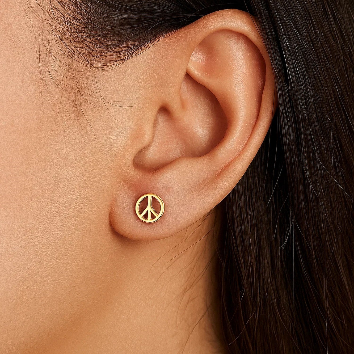 A single 14k yellow gold peace sign stud earring is worn on an ear.