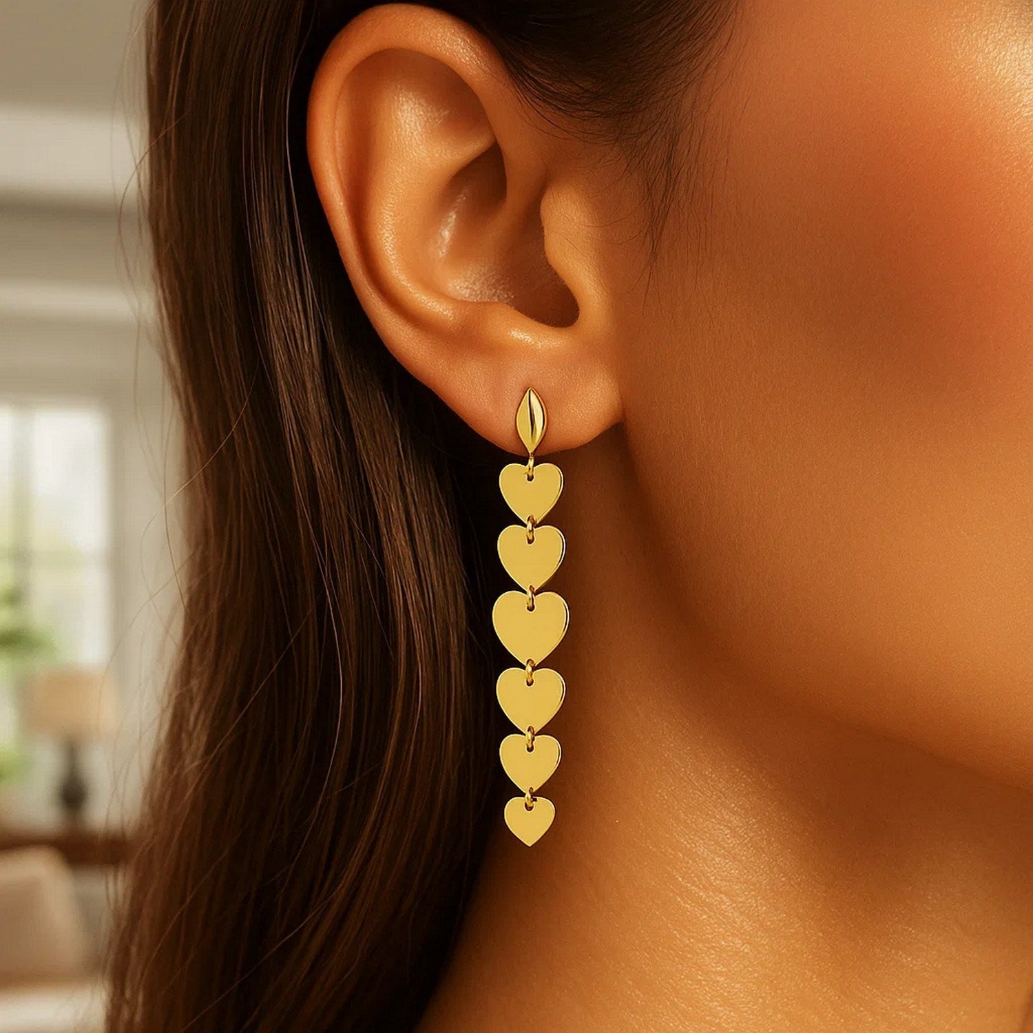 14K yellow gold heart drop earrings are shown on a woman's ear.