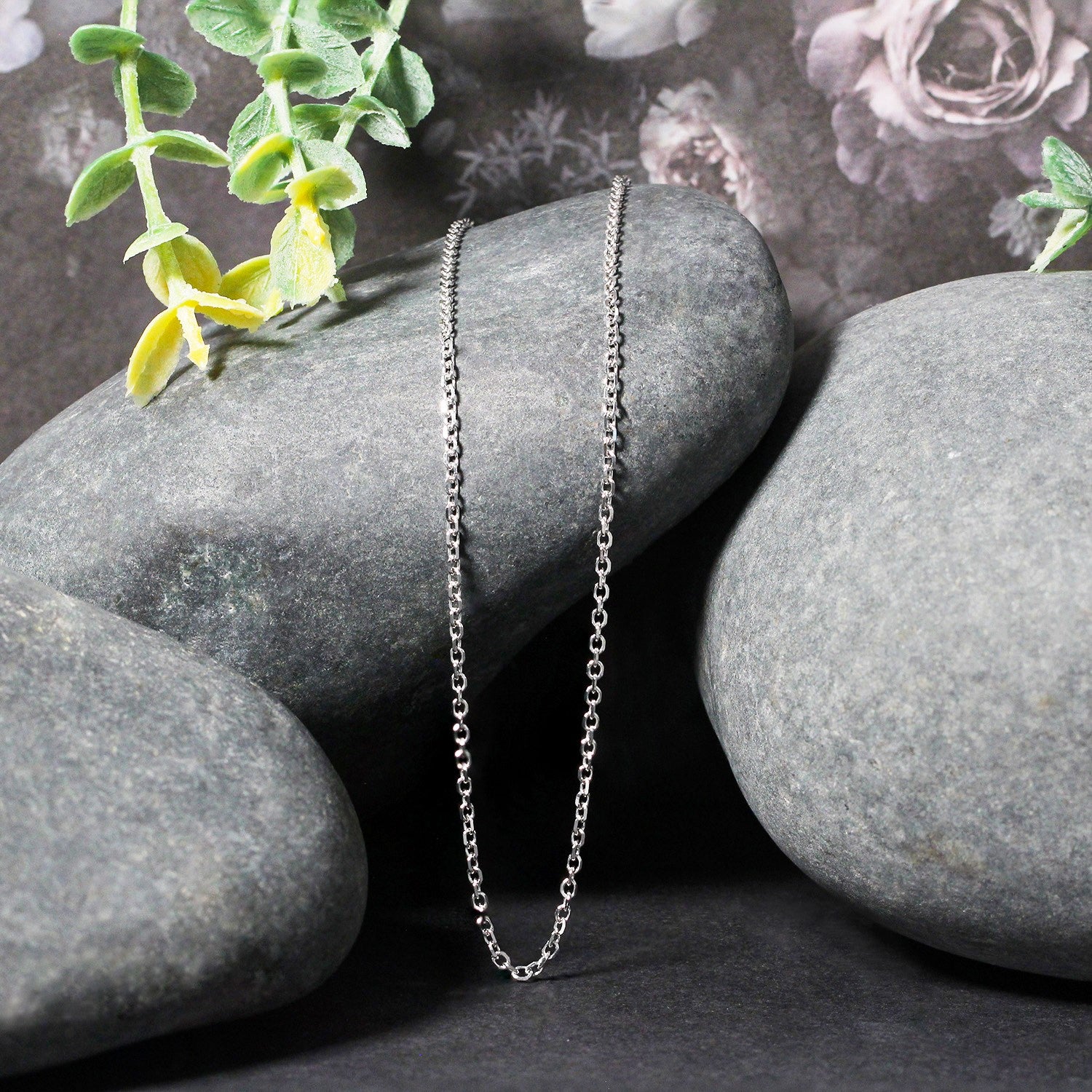An 18k white gold diamond cut cable link chain rests on a grey stone.