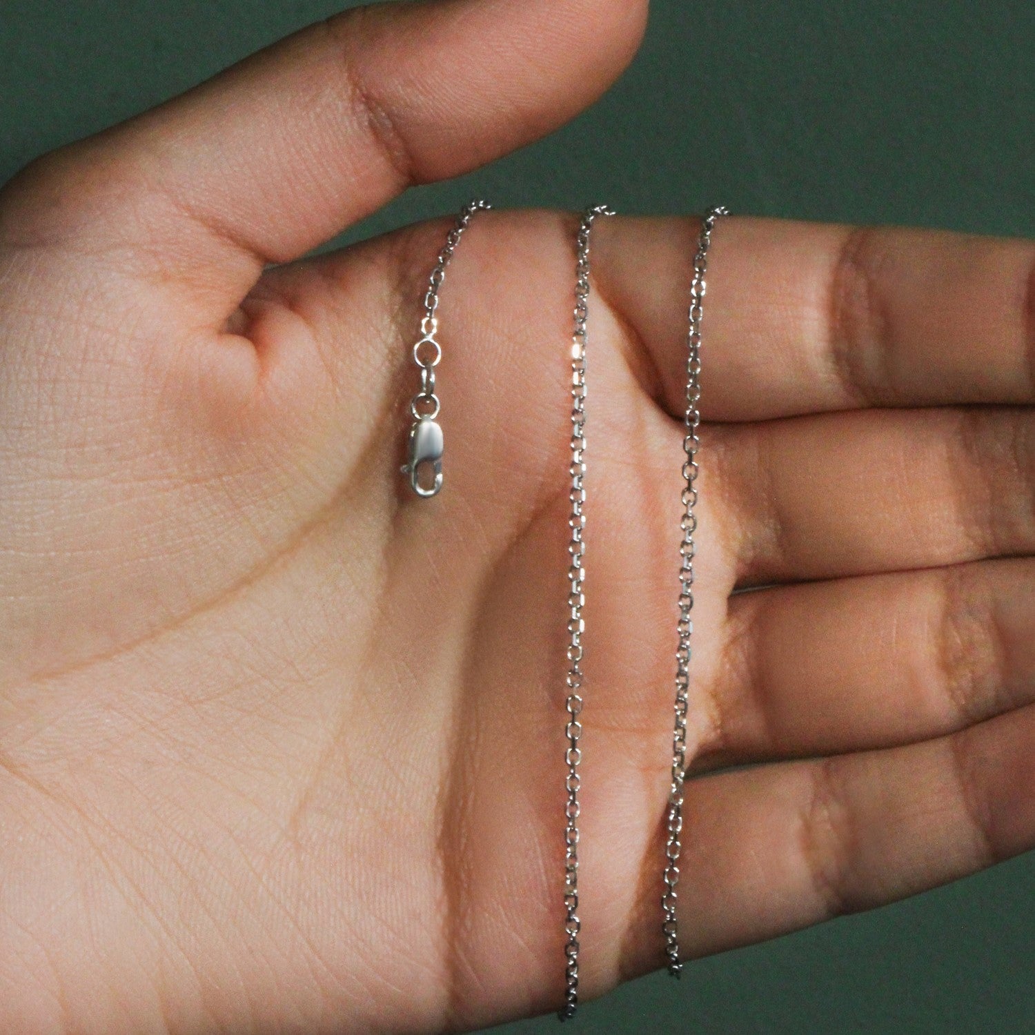 18k white gold diamond cut cable link chain with a lobster clasp, held in a hand.