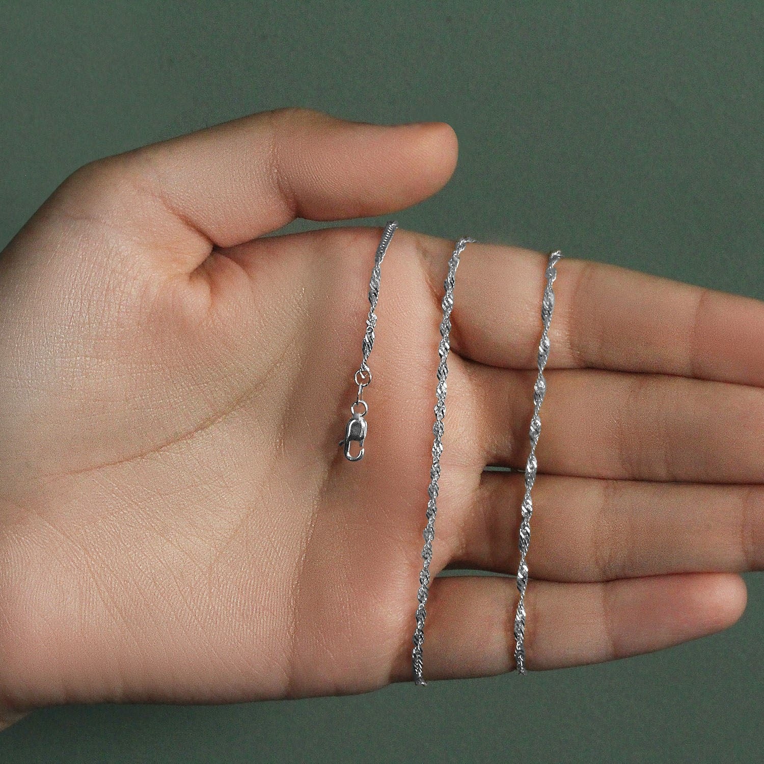 14k white gold Singapore chain with a lobster clasp held in a hand.