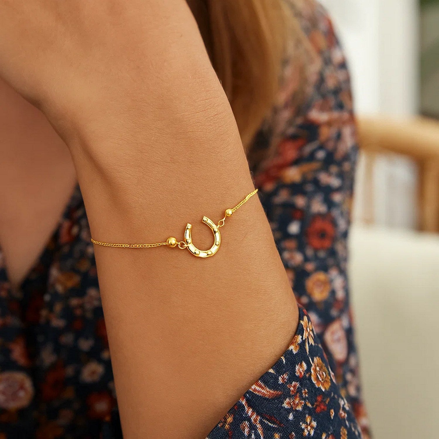 Adjustable 14K yellow gold horseshoe drawstring bracelet on a woman's arm.