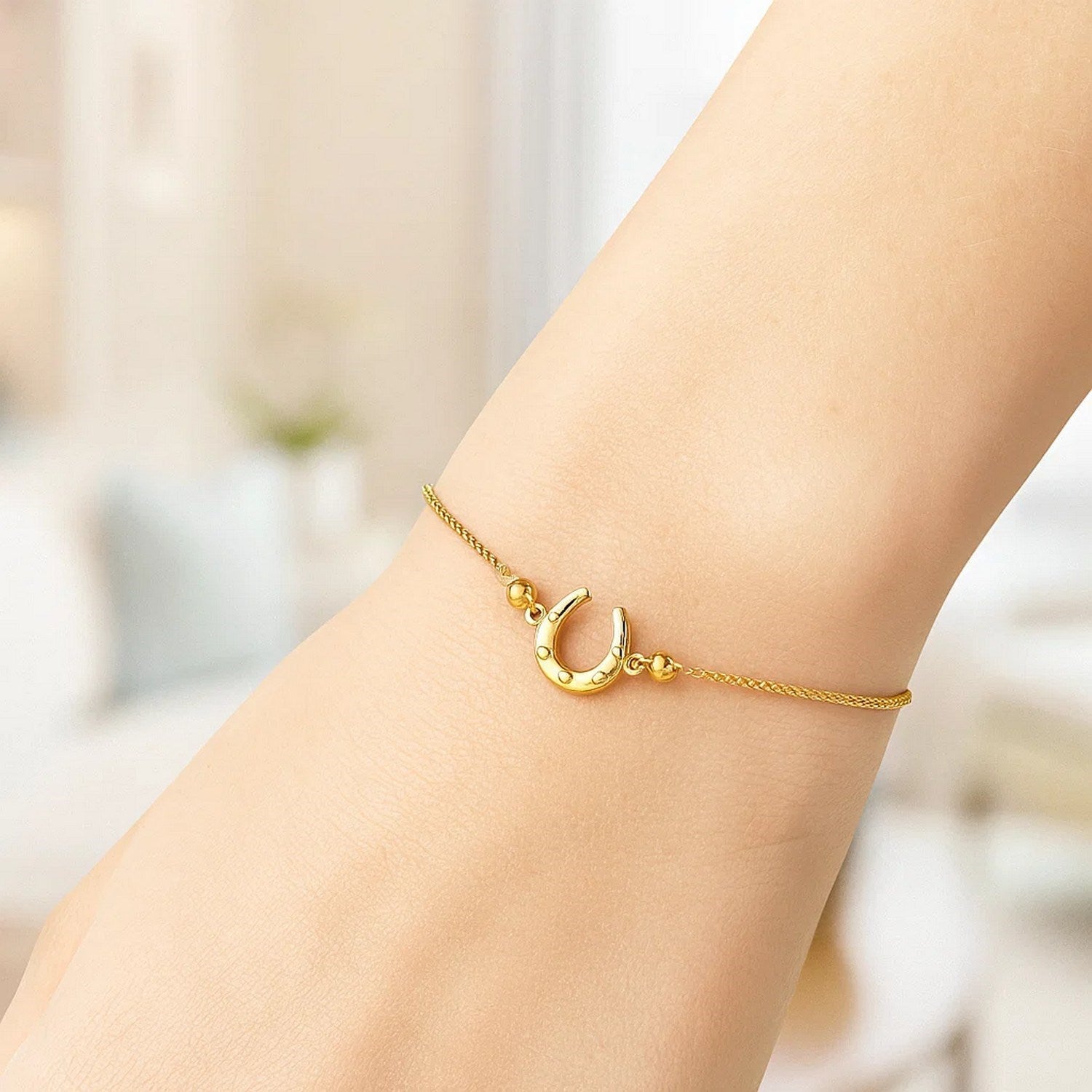 Adjustable 14K yellow gold horseshoe drawstring bracelet on a person's wrist.