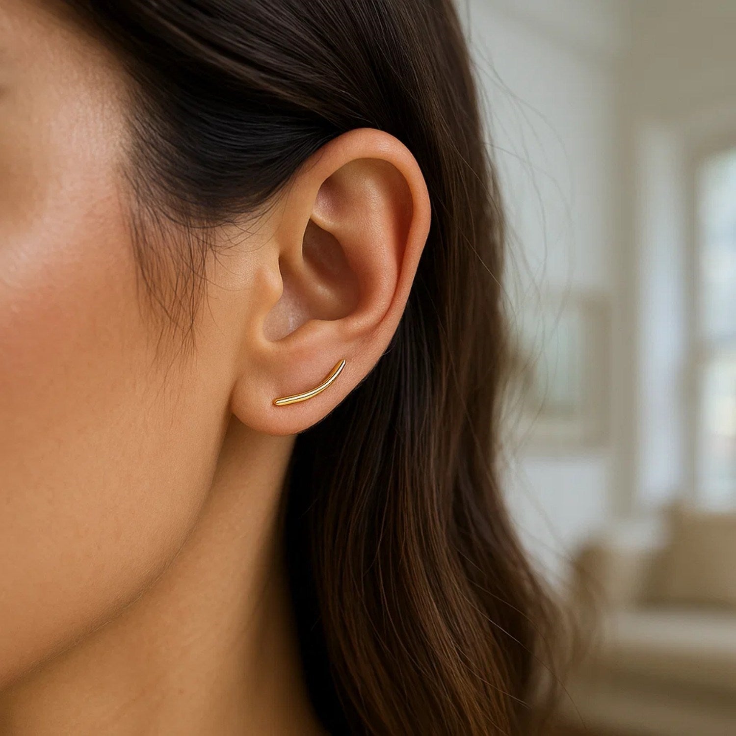 A woman wears a single 14k yellow gold curve climber post earring.
