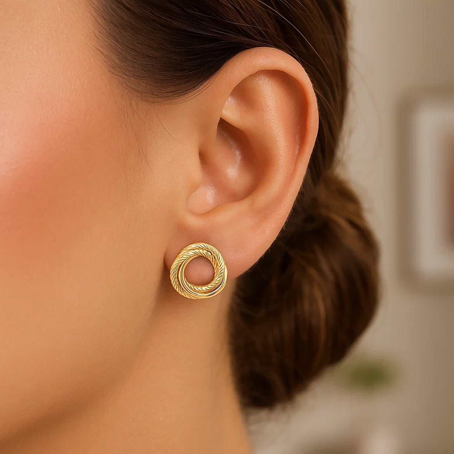 14K yellow gold diamond-cut interlocking trinity stud earring on an ear.