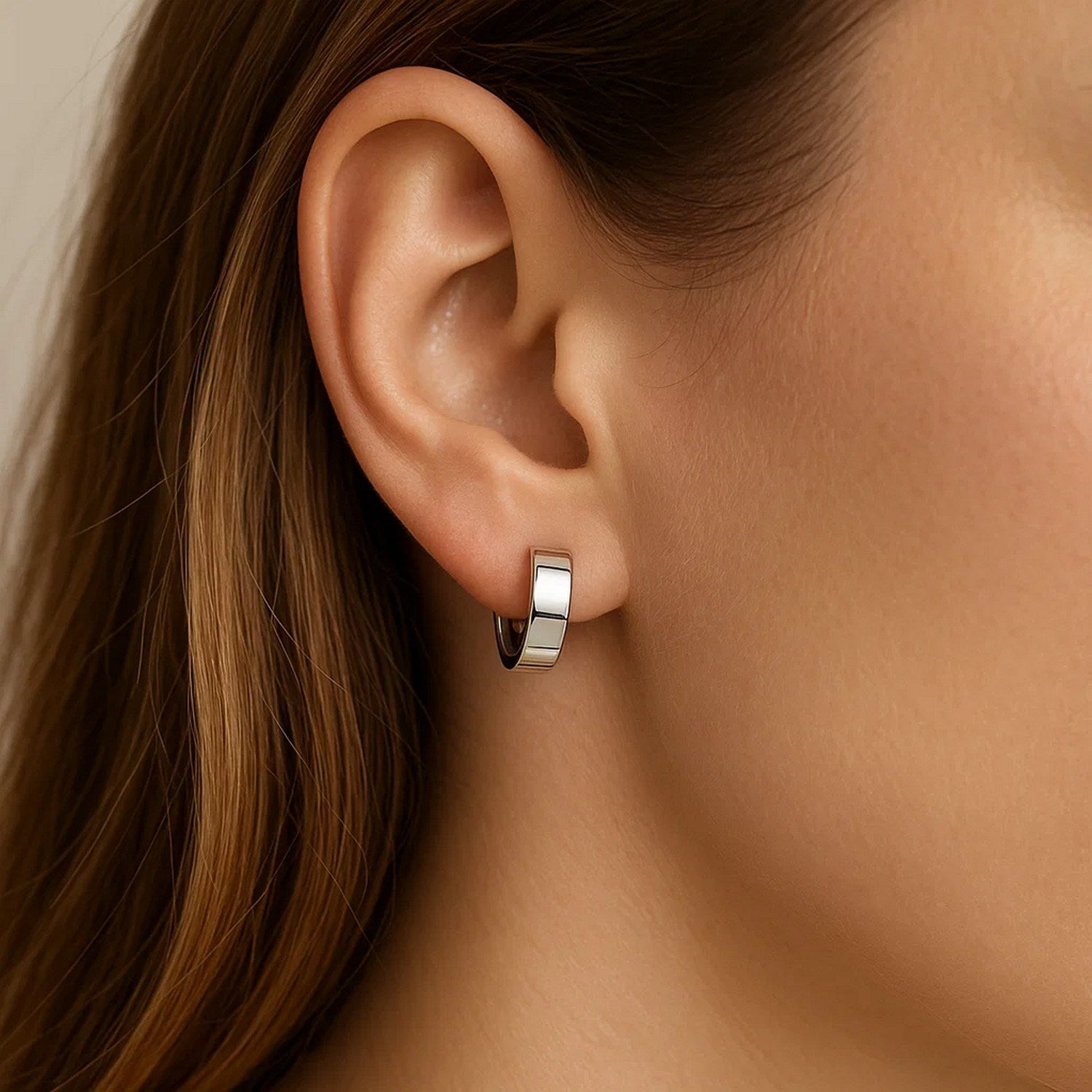 A woman wears a single 10k white gold snuggable hoop earring.