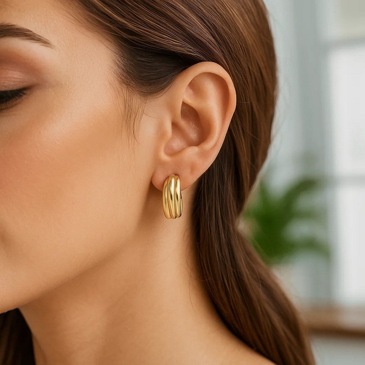 14K yellow gold ribbed hoop earrings are worn on a woman's ear.
