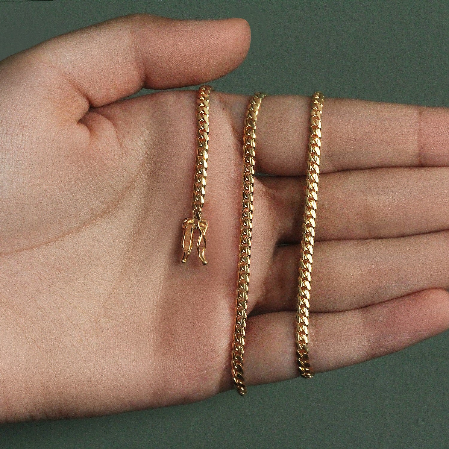 A 10k yellow gold classic solid Miami Cuban chain with a box catch clasp on a hand.
