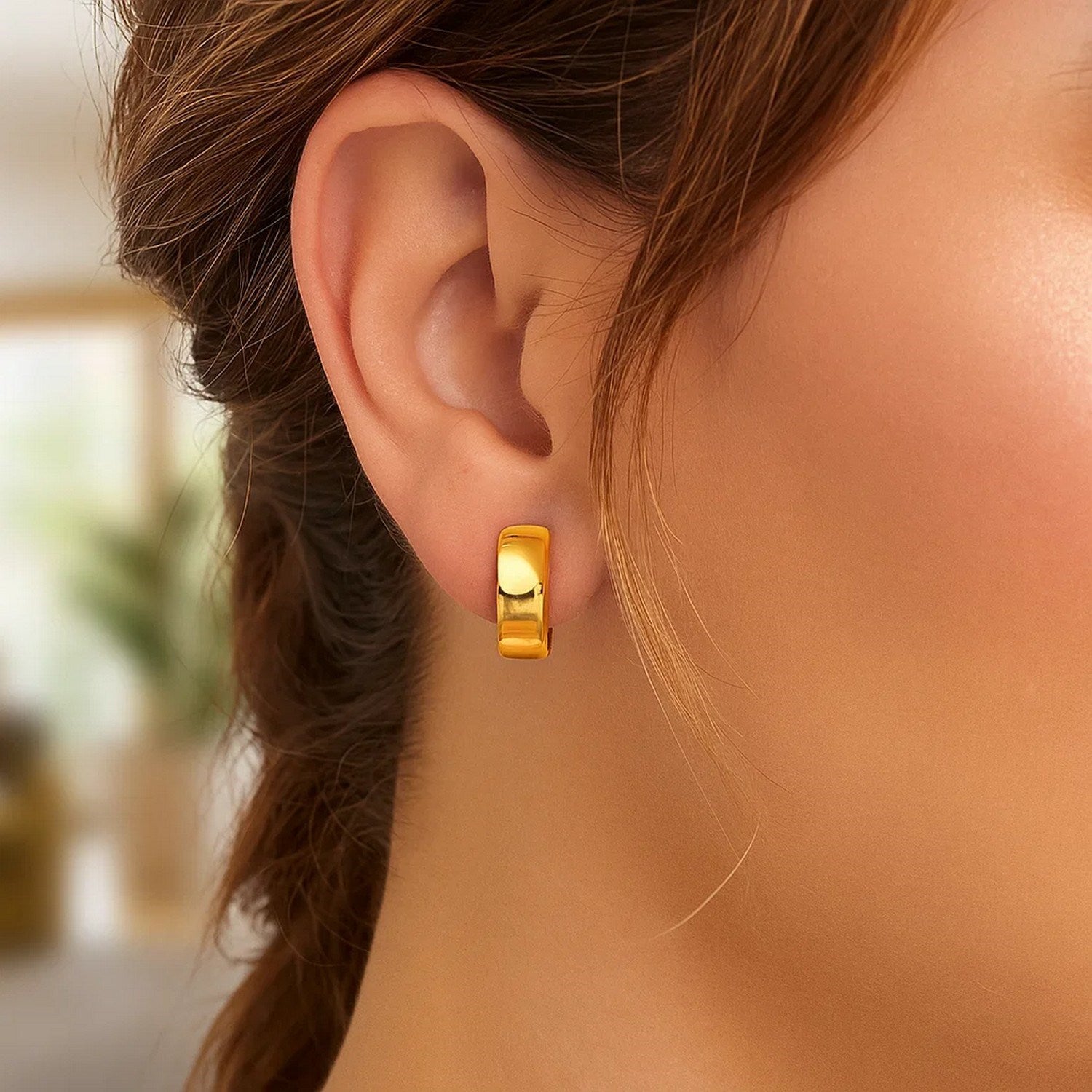 A woman wears a single 14k yellow gold textured and polished hoop earring.